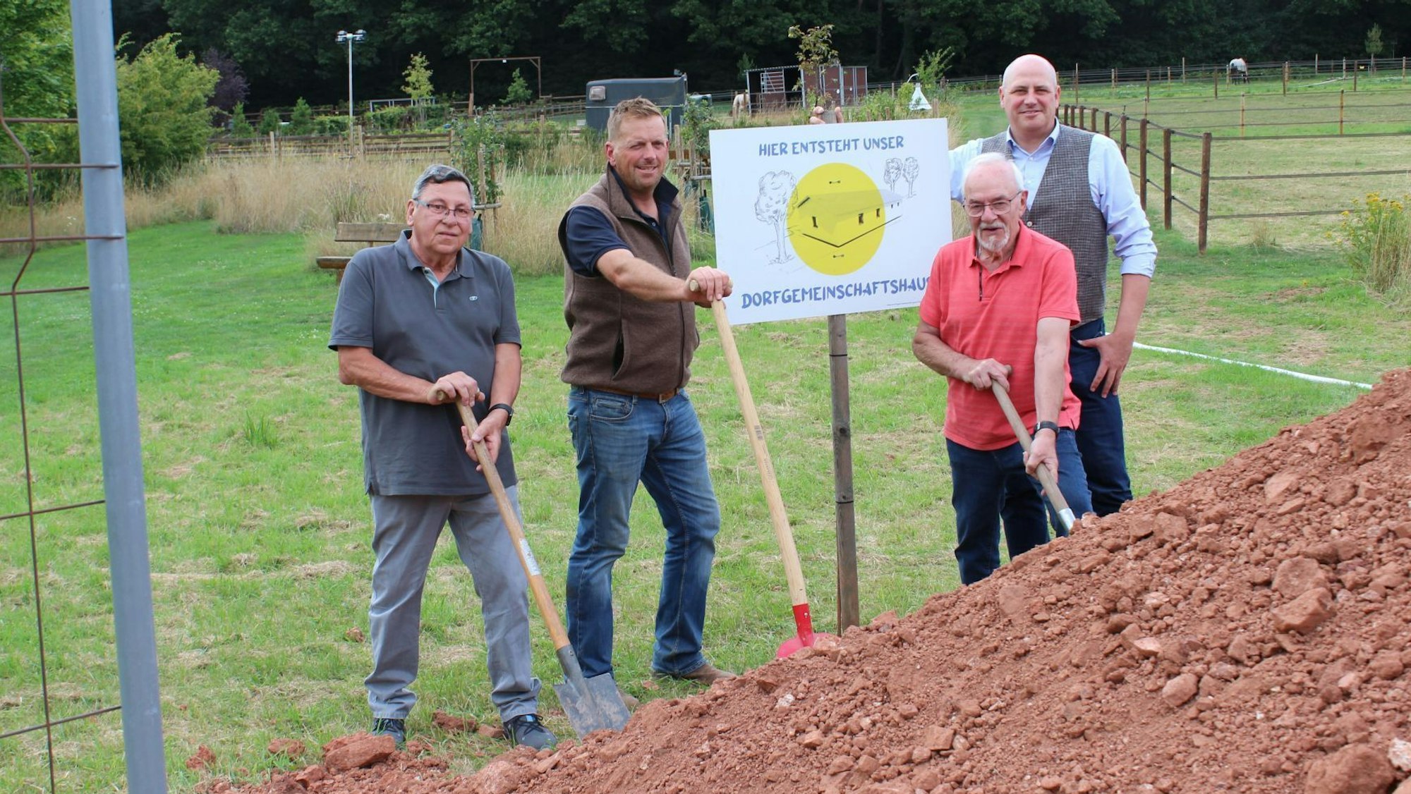 Vier Männer stehen mit Spaten an einem Erdhügel und schauen in die Kamera.