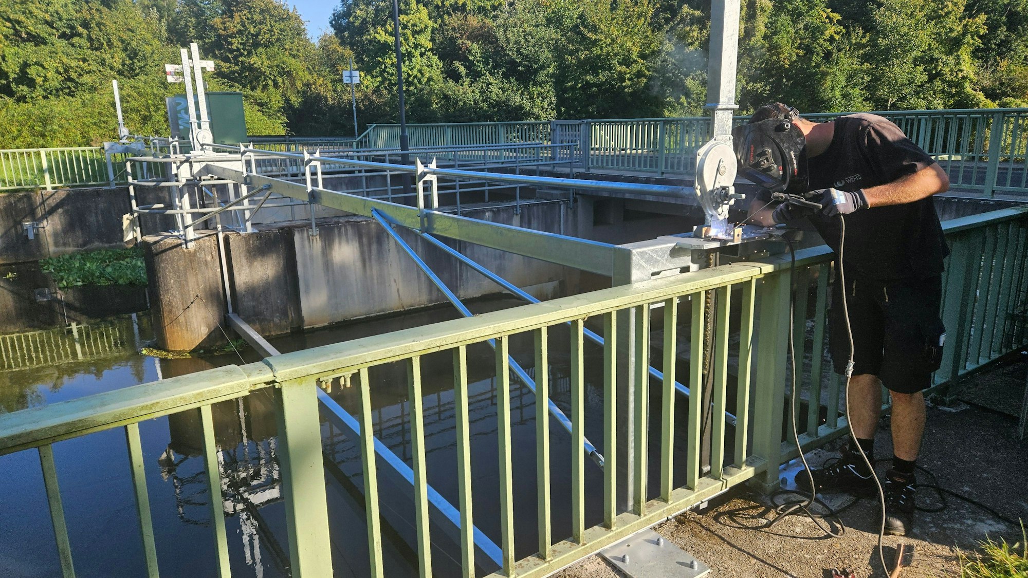 Ein Metallbauer arbeitet an einer Konstruktion an einem Wehr in der Erft.