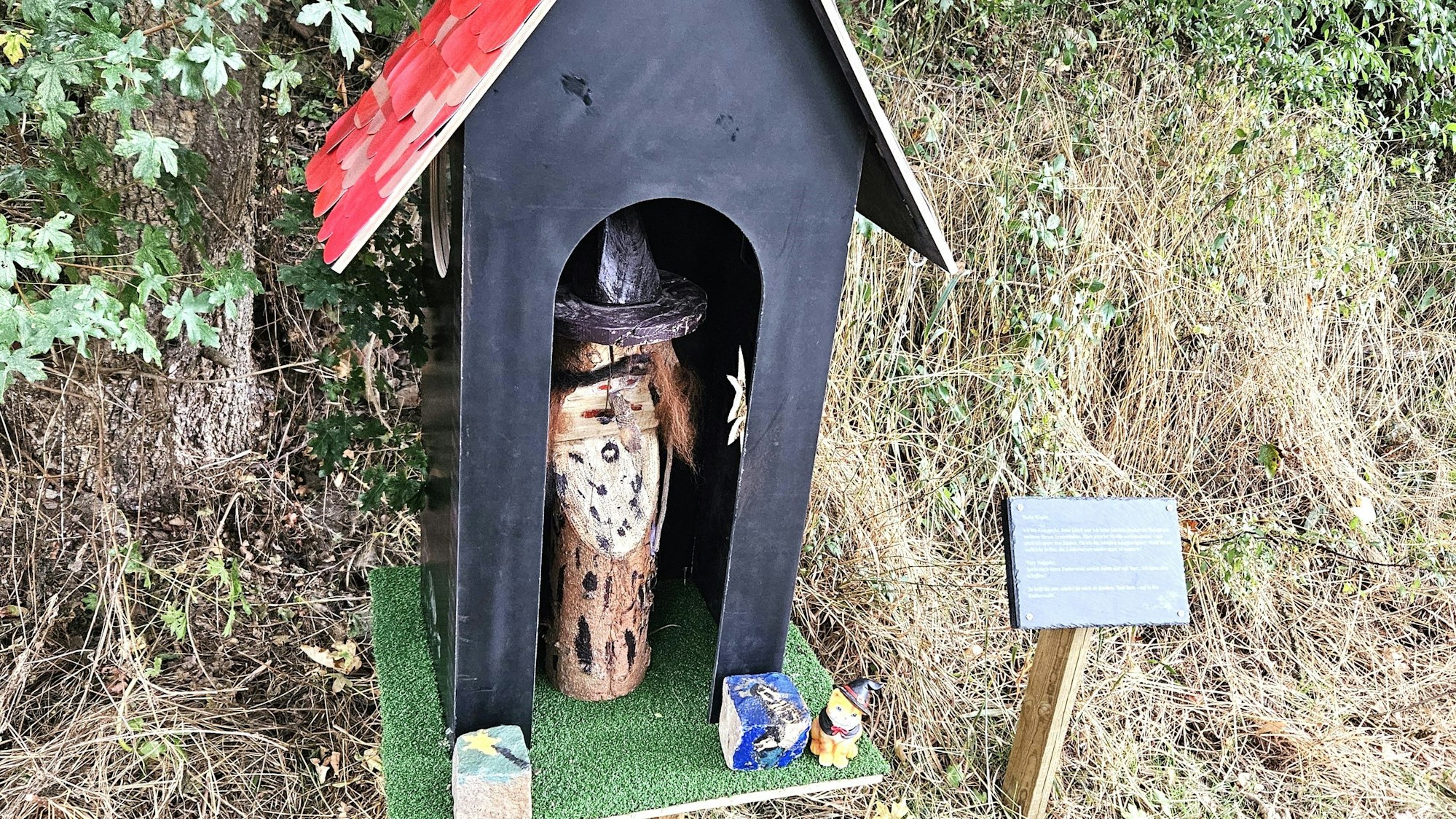 Hexe Toscanella steht in einem schwarzen Haus mit rotem Dach.