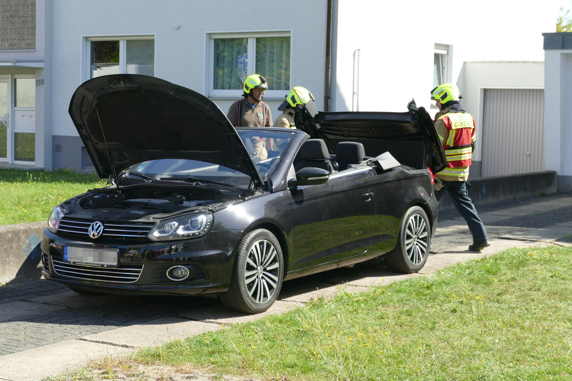 Einsatzkräfte der Feuerwehr an einem schwarzen Cabriolet mit Metallklappdach.