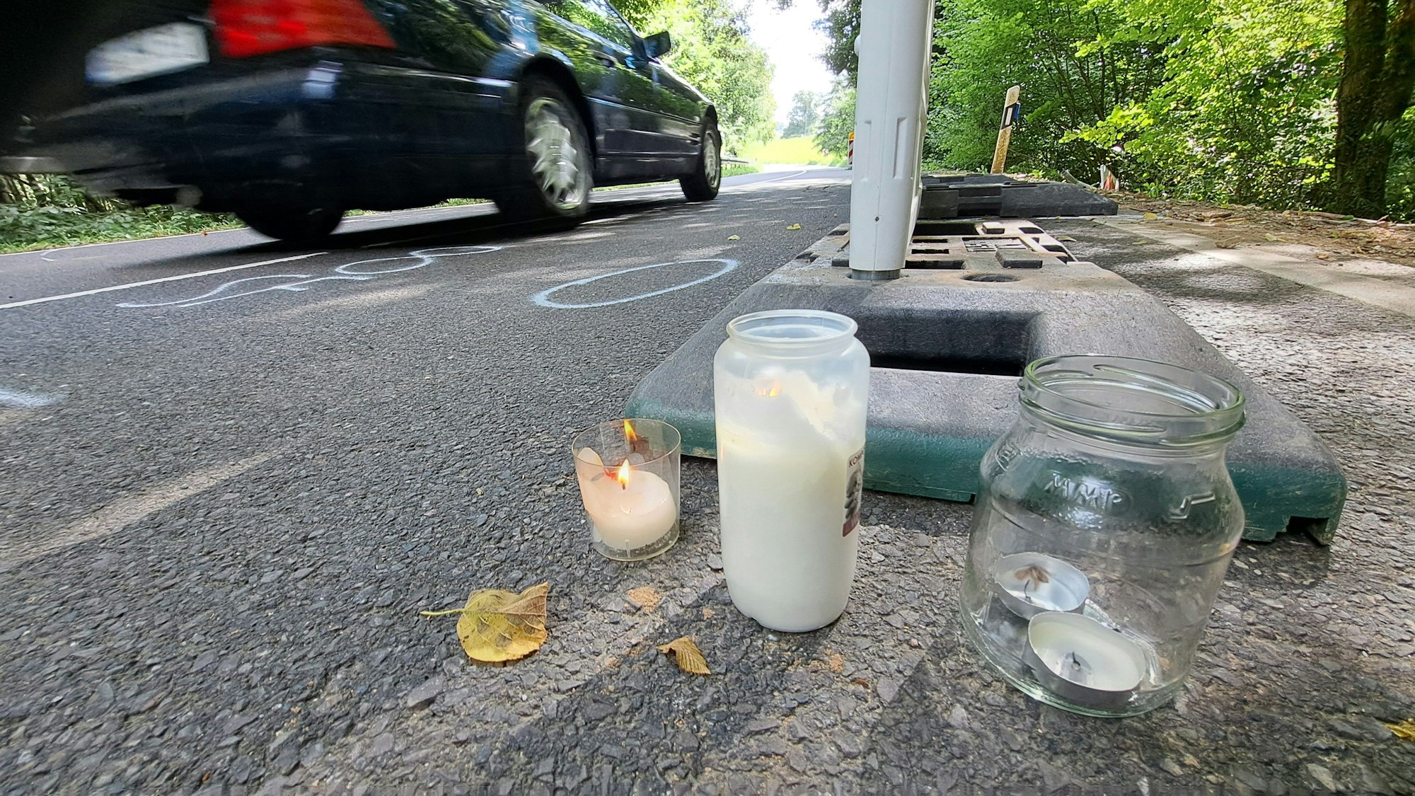 Zwischen Warnbaken stehen Kerzen auf der Dürschtalstraße, auf der sich am Samstag (16.8.) ein tödlicher Unfall ereignet hat, bei dem vier Teenager im Alter von 14 bis 19 Jahren ums Leben kamen.