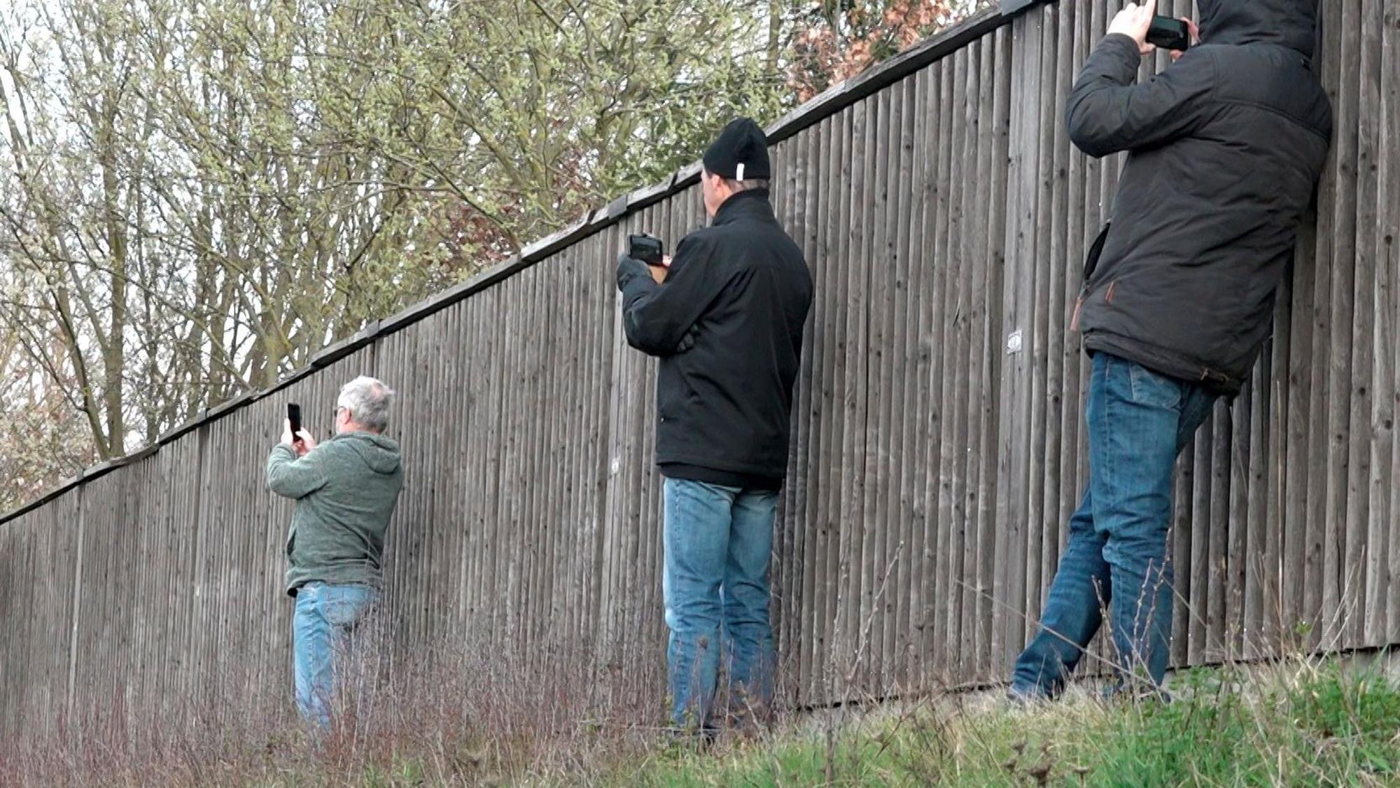 Schaulustige fotografieren neben einer Lärmschutzwand mit ihren Smartphones eine Unfallstelle.