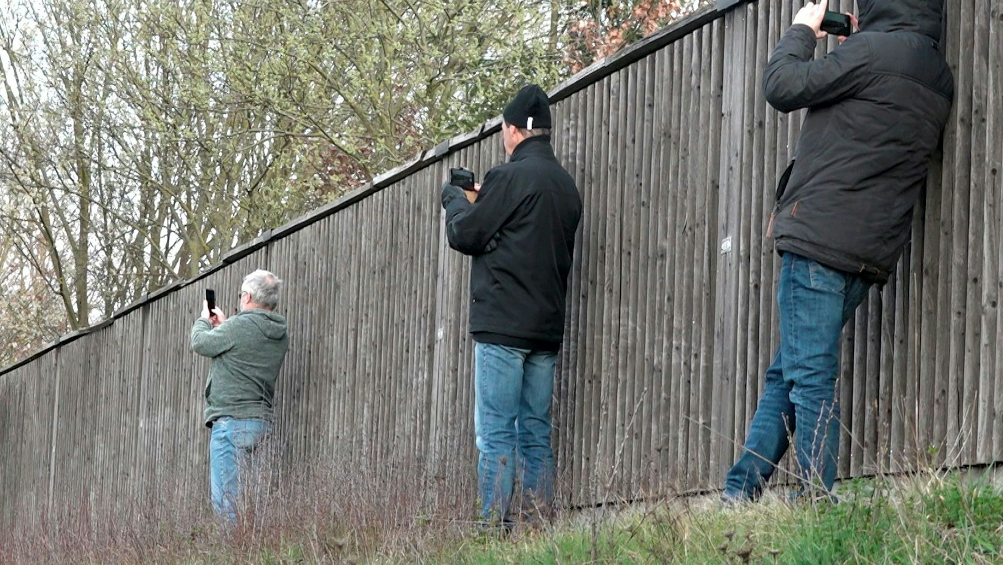 Schaulustige fotografieren neben einer Lärmschutzwand mit ihren Smartphones eine Unfallstelle.
