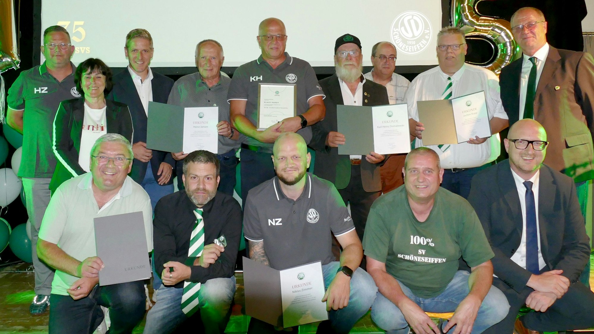 Die Gehrten knien und stehen in zwei Reihen hintereinander. Auf einer Leinwand dahinter ist 75 Jahre SV Schöneseiffen 1950 zu lesen.