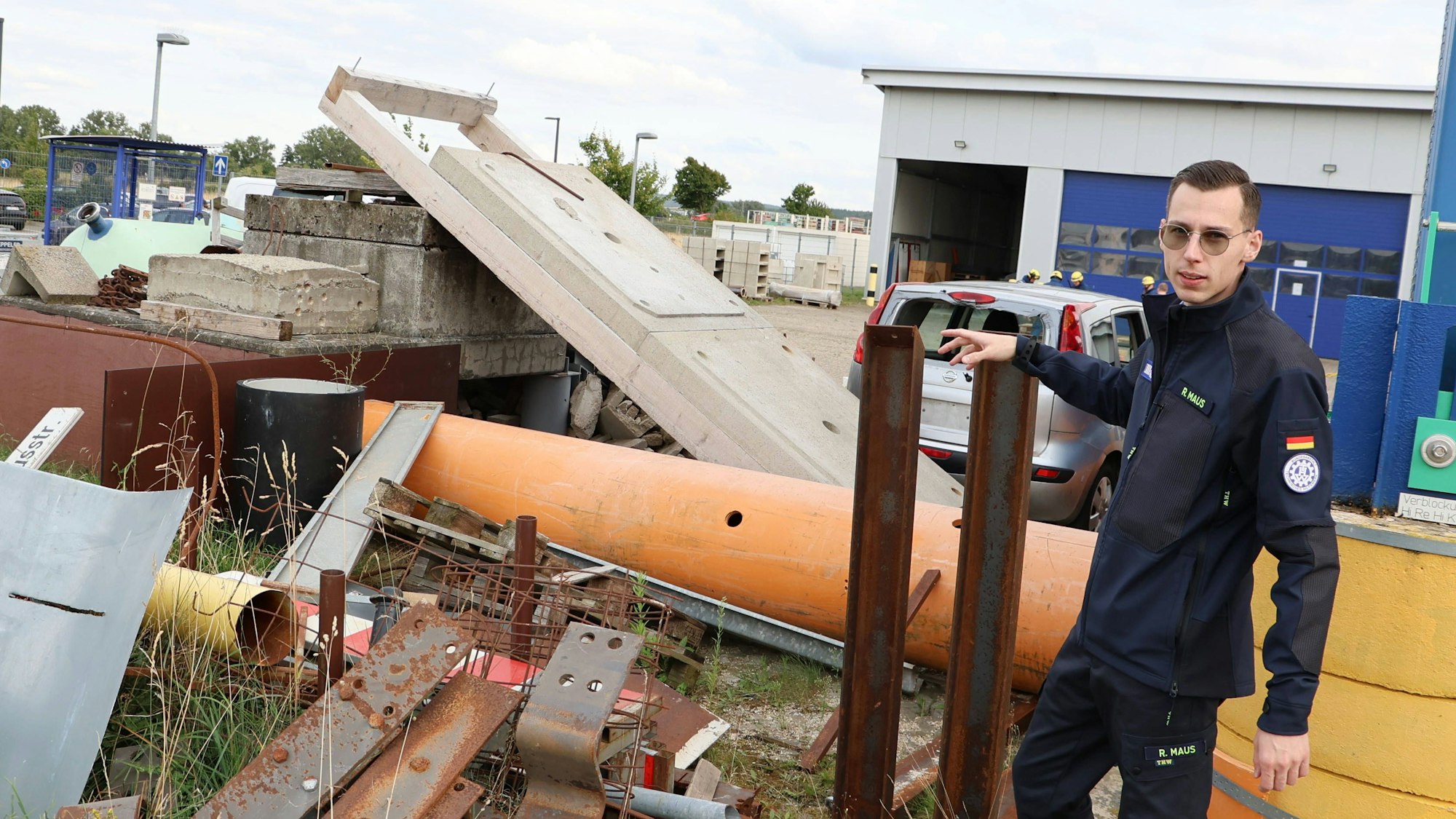 Raphael Maus zeigt auf Metalle, Rohre und Steine, die auf dem Übungsgelände stehen.