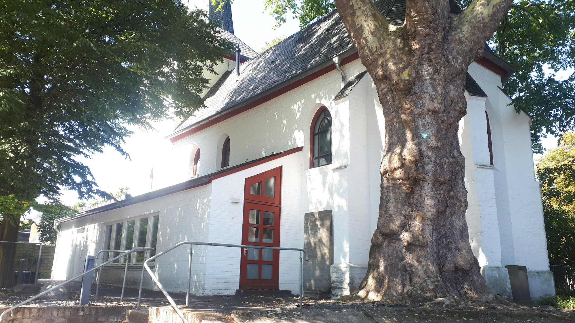 Eine weiß getünchte kleine Kirche steht hinter einem mächtigen alten Baum.