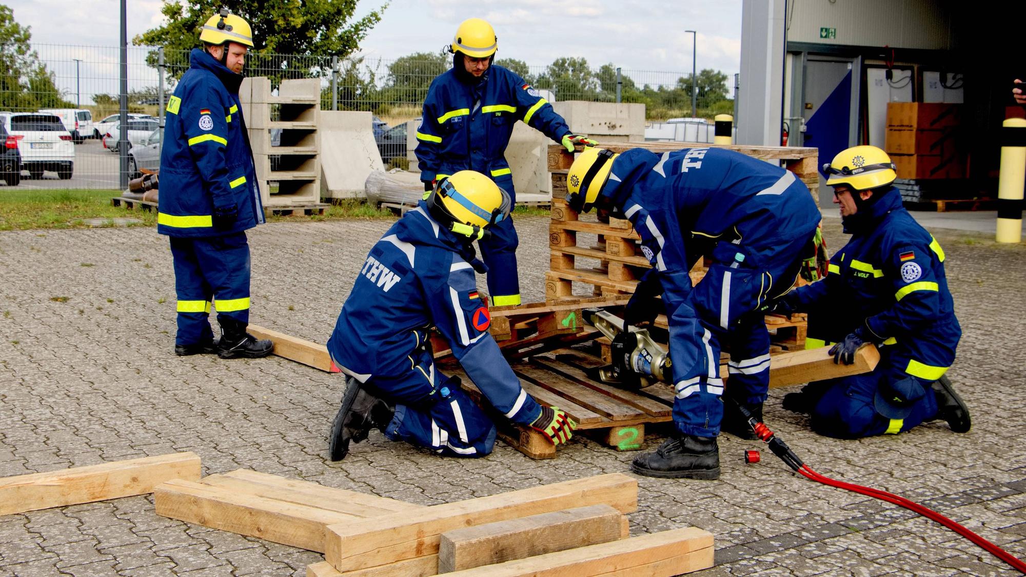 Fünf Einsatzkräfte in blauen THW-Uniformen üben an Holzpaletten.