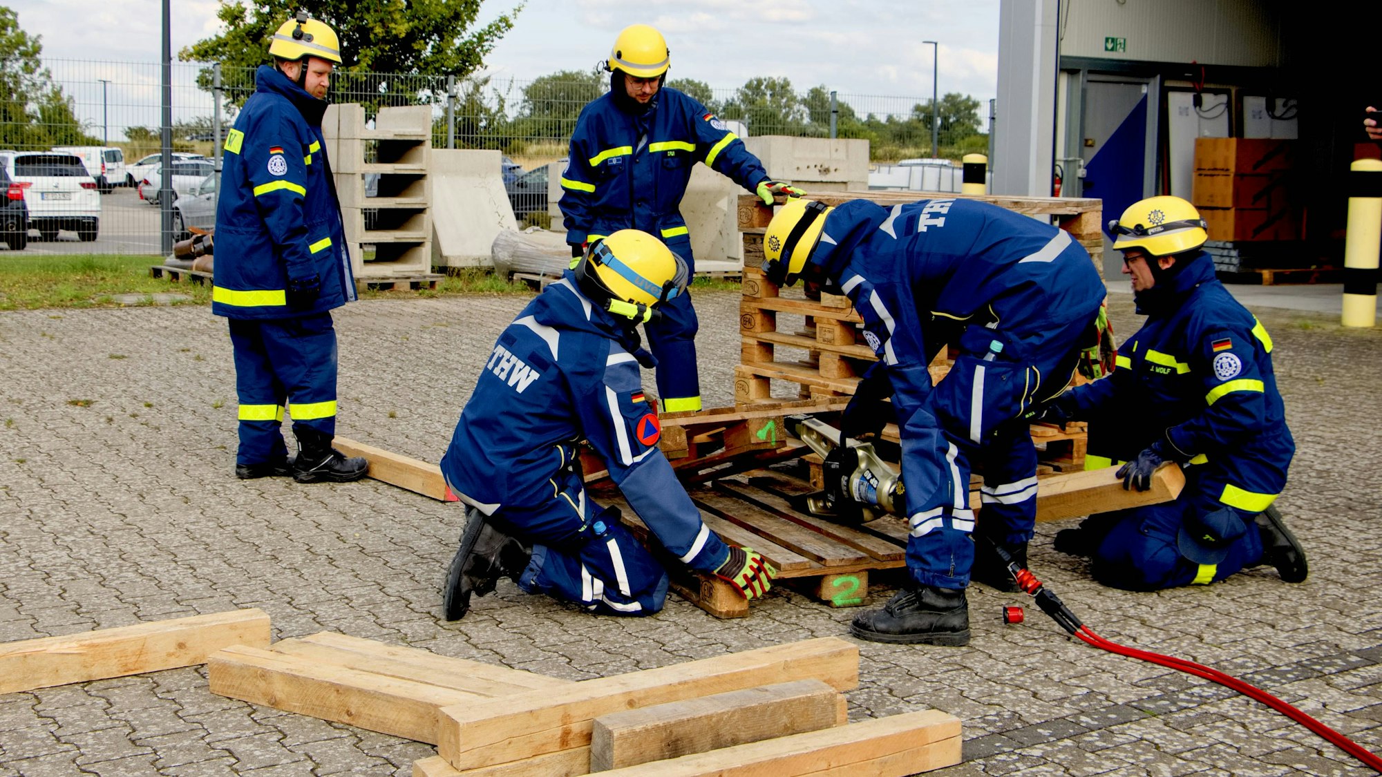 Fünf Einsatzkräfte in blauen THW-Uniformen üben an Holzpaletten.