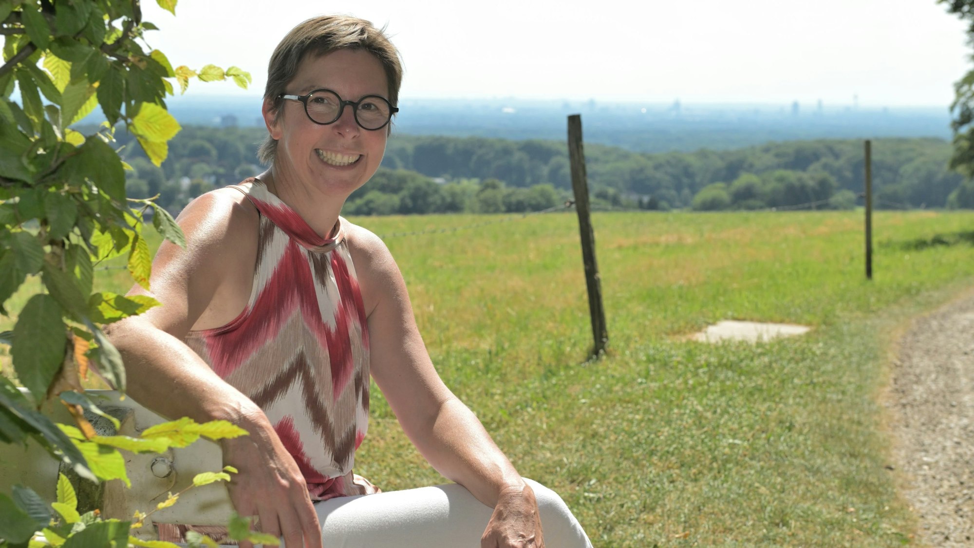 Bürgermeisterkandidatin Sonja Tewinkel (parteilos) sitzt auf einer Bank in der Sonne. Im Hintergrund die Kölner Bucht.