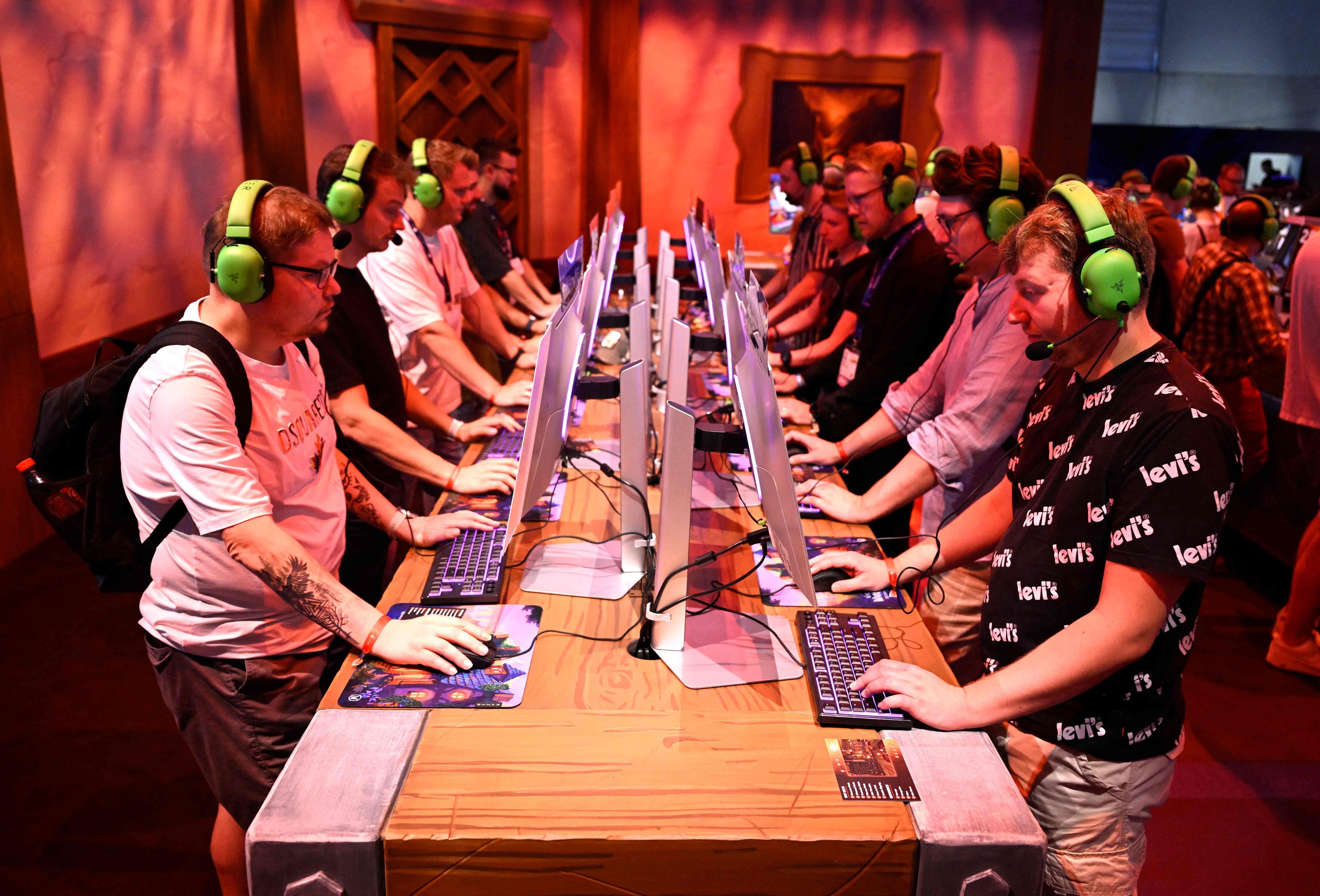 Am ersten Tag der Gamescom 2025: Besucher testen das Videospiel „World of Warcraft Midnight“. Sie sitzen jeweils vor einem Computer und tragen neongrüne Headsets.