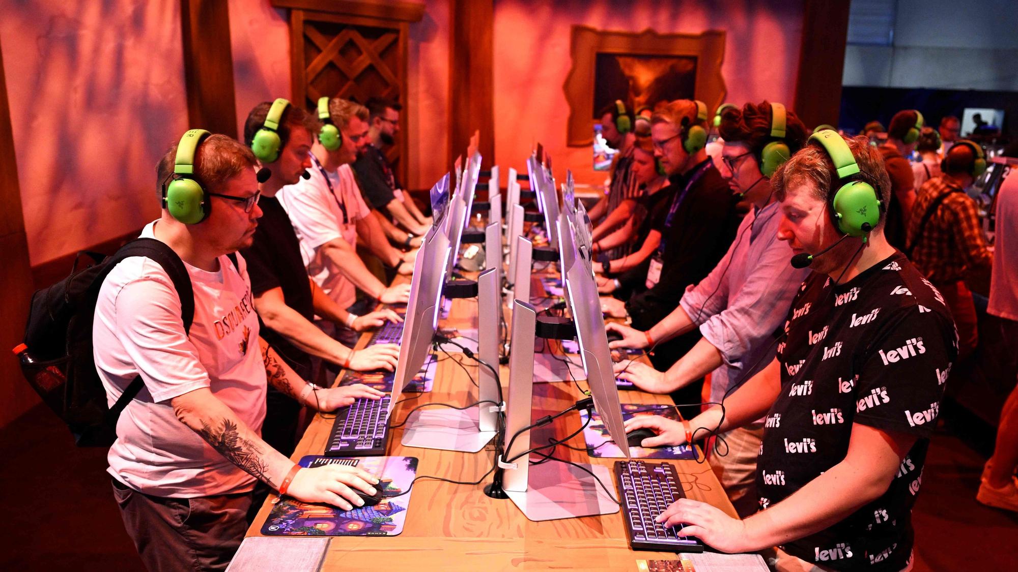 Am ersten Tag der Gamescom 2025: Besucher testen das Videospiel „World of Warcraft Midnight“. Sie sitzen jeweils vor einem Computer und tragen neongrüne Headsets.