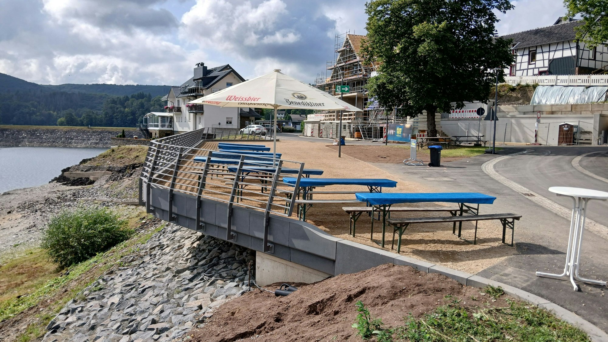 Auf einem balkonähnlichen Gelände am Rursee stehen Bänke, Tische und ein Sonnenschirm.