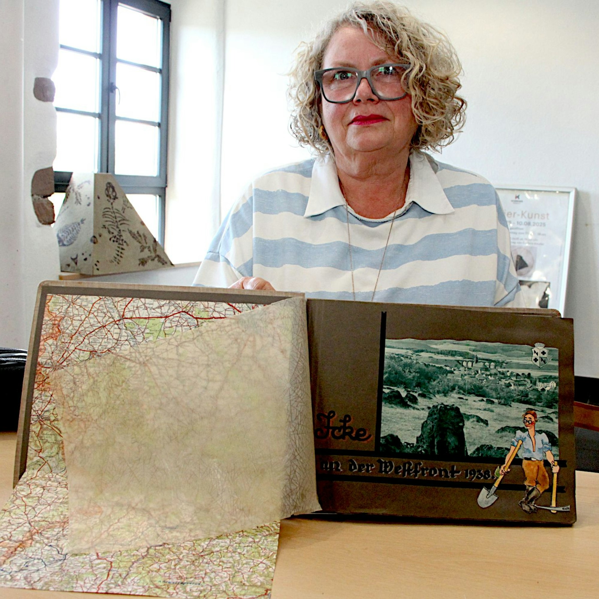 Claudia Warda zeigt das Album, in das auch eine Karte geklebt ist. Neben ein Foto hat jemand einen Mann mit Hacke und Schaufel gemalt.