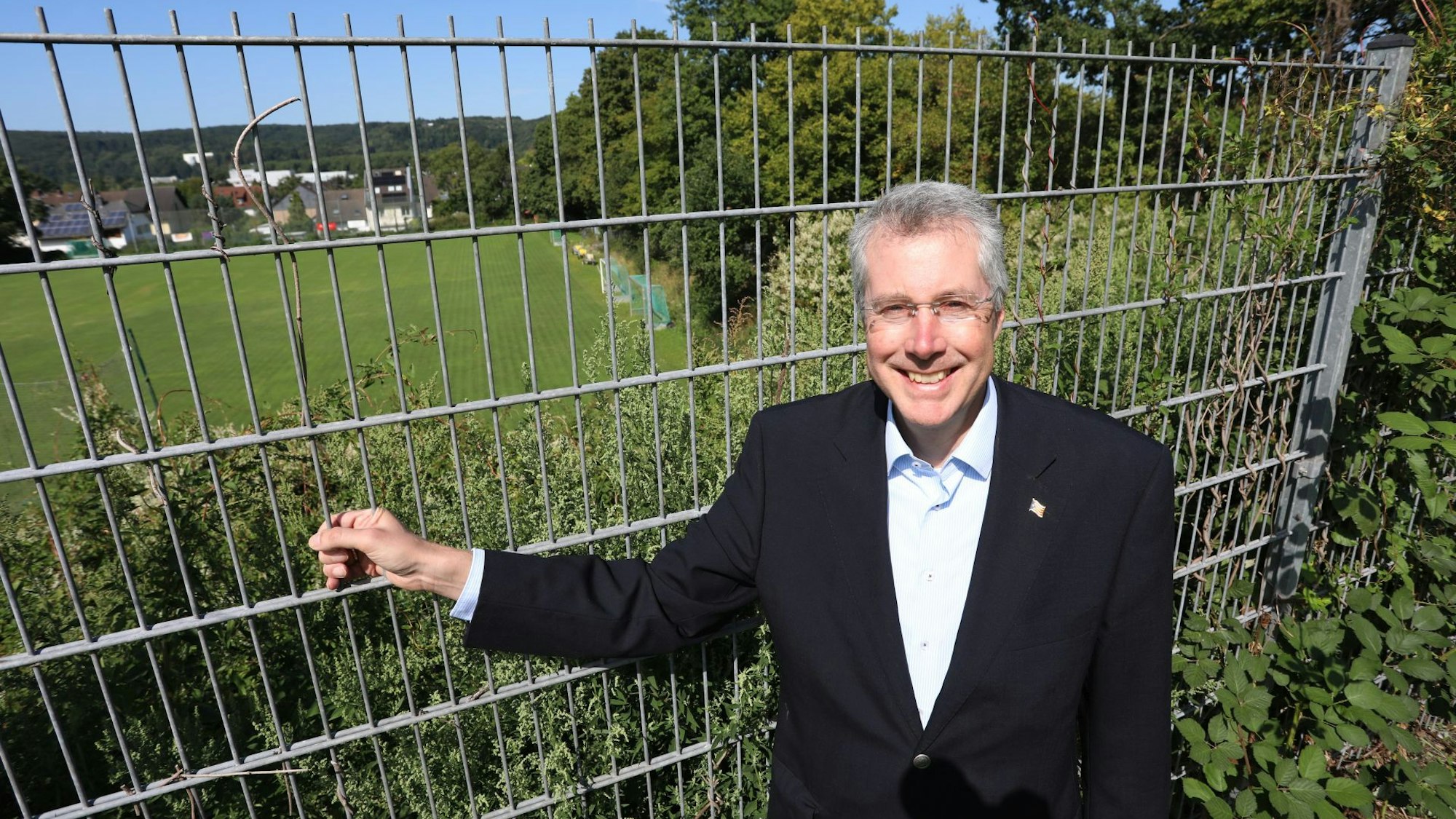 Ein Mann an einem Zaun, im Hintergrund eine große Wiese.