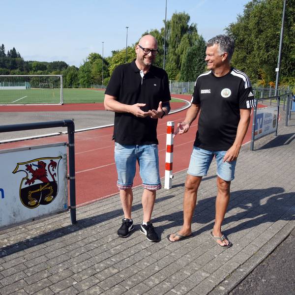Vorsitzender Andre Vicariesmann und Geschäftsführer Jörg Müller stehen an einem Sportplatz.