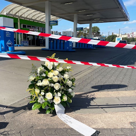 22.08.2025, Saarland, Völklingen: An der Tankstelle, an der nach einem Überfall ein Polizist getötet wurde, haben Mitarbeiter einen Kranz niedergelegt. Nach einem Raubüberfall auf die Tankstelle ist ein Polizist durch Schüsse getötet worden. Nach Angaben der Polizei hatte der mutmaßliche Täter dem Beamten bei einem Gerangel die Dienstwaffe entrissen und geschossen. Foto: Christian Schultz/dpa +++ dpa-Bildfunk +++