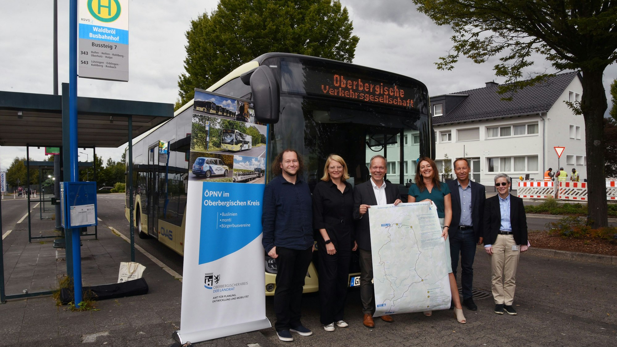 Fünf Menschen stehen am Bahnhof in Waldbröl vor einem Bus und halten ein Plakat hoch.