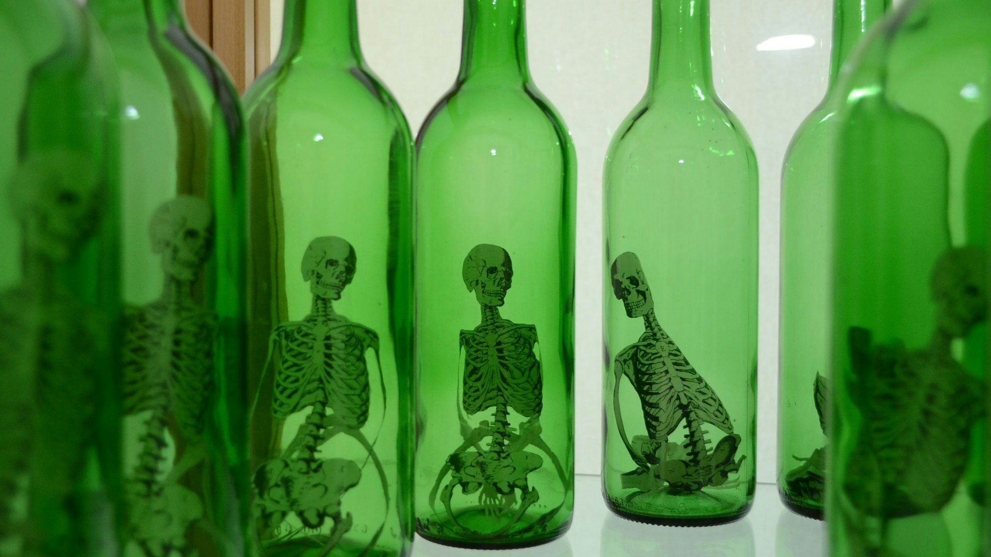 Flaschen aus grünem Glas; in den Flaschen sieht man kleine menschliche Skelette aus Papier.