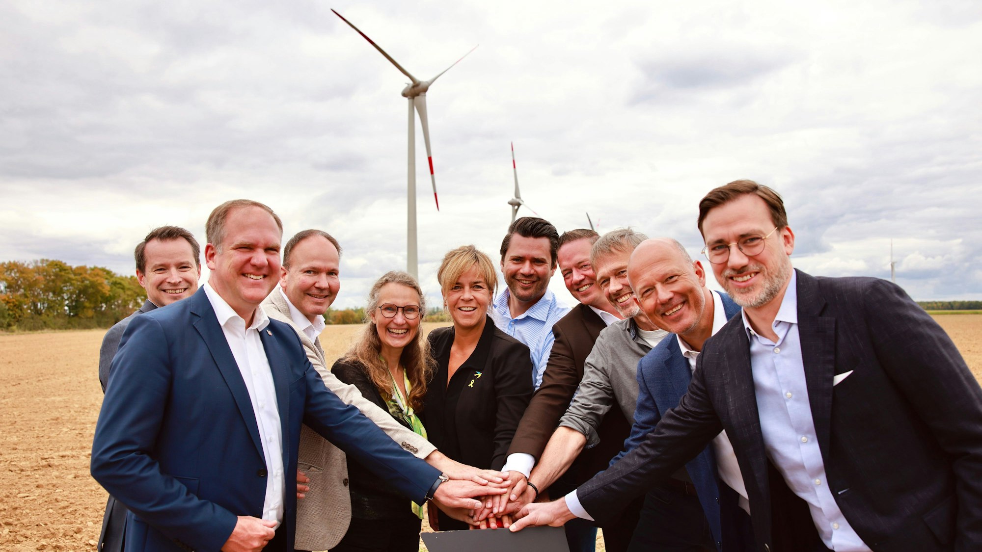 Das Foto zeigt die Vertreter der Unternehmen und aus der Politik beim symbolischen Knopfdruck, im Hintergrund die Windräder.