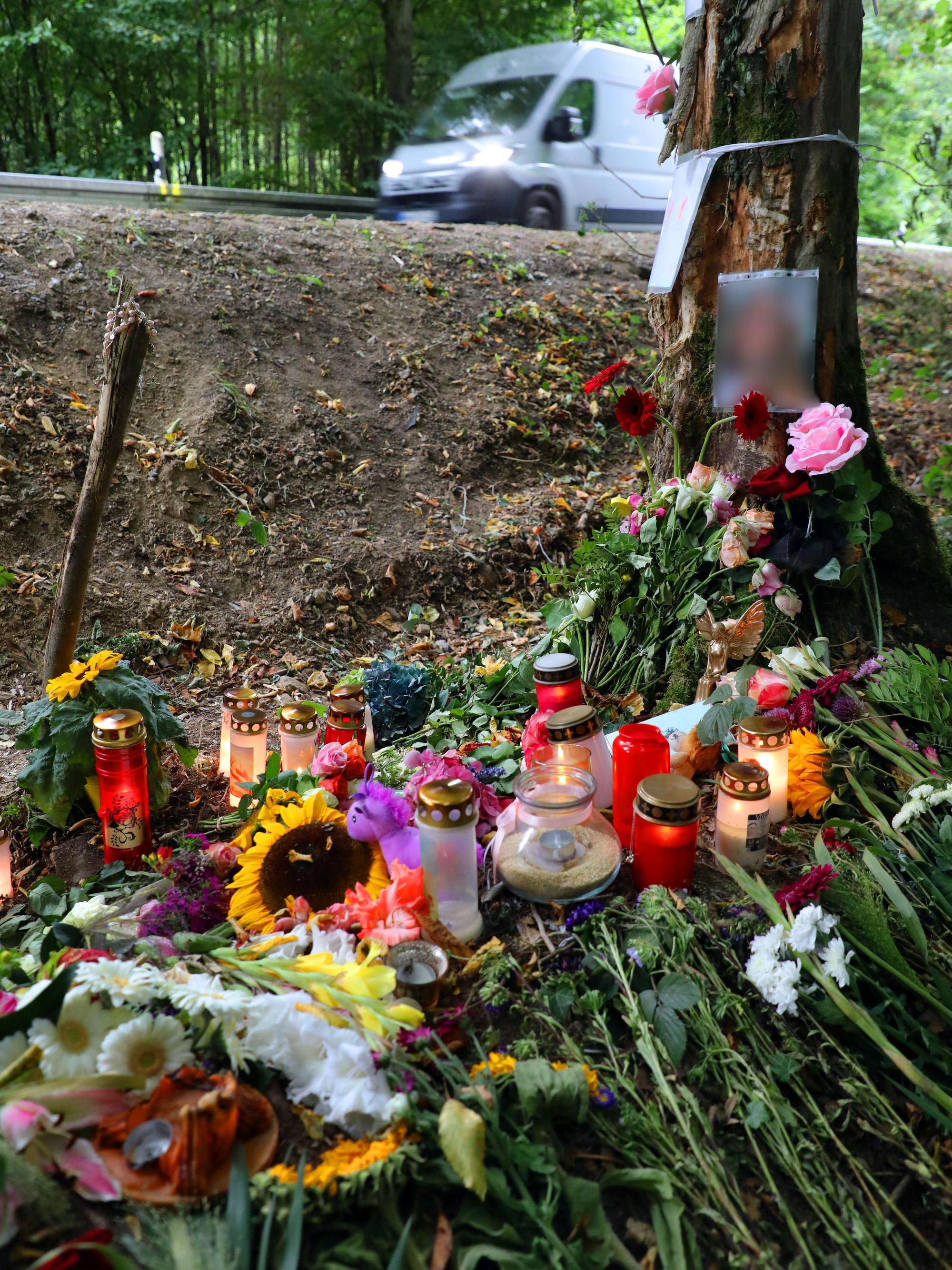 Blumen und Kerzen liegen und stehen in der Kurve, in der am 16. August 2026 vier Teenager bei einem Unfall ums Leben kamen.
