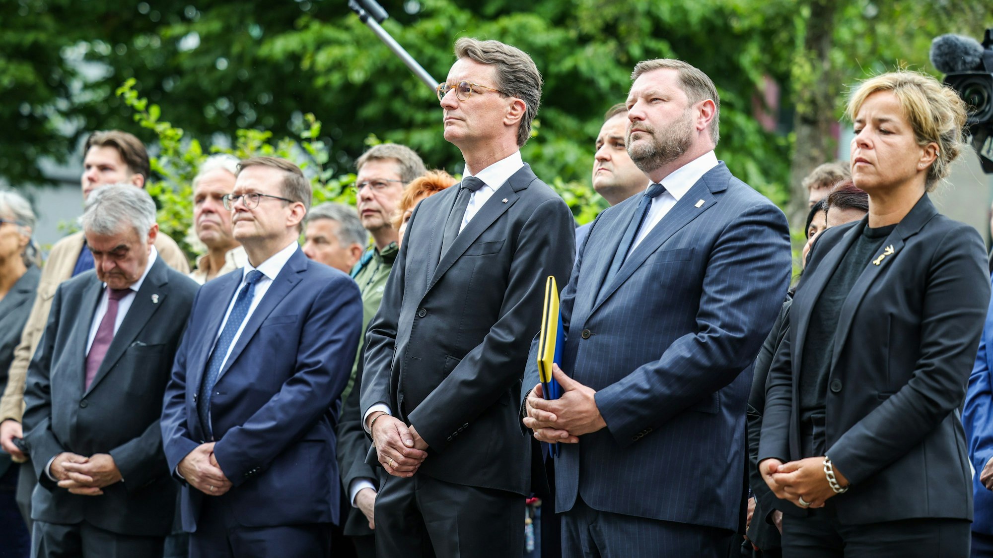 NRW-Innenminister Herbert Reul (CDU, l), Ministerpräsident Hendrik Wüst (3.v.r, CDU), Tim Kurzbach (2.v.r, SPD), Oberbürgermeister der Stadt Solingen und NRW-Wirtschaftsministerin Mona Neubaur (r, Bündnis 90/Grüne) stehen zusammen bei der Gedenfeier in Solingen.