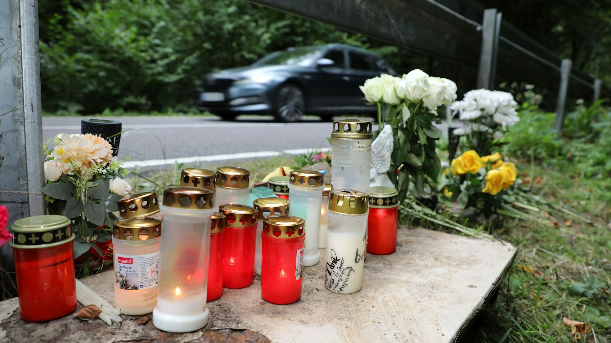 Kerzen stehen am Wegesrand, während ein Auto vorbeirauscht.