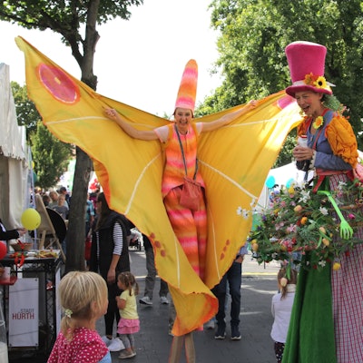 Das Foto zeigt zwei bunt kostümierte Frauen auf Stelzen vor dem Medio.