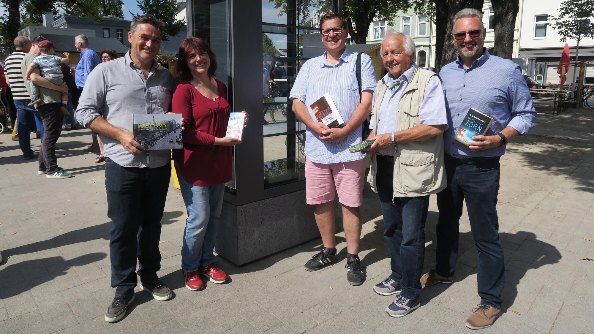 Fünf Menschen stehen links und rechts von einem nagelneuen Bücherschrank.