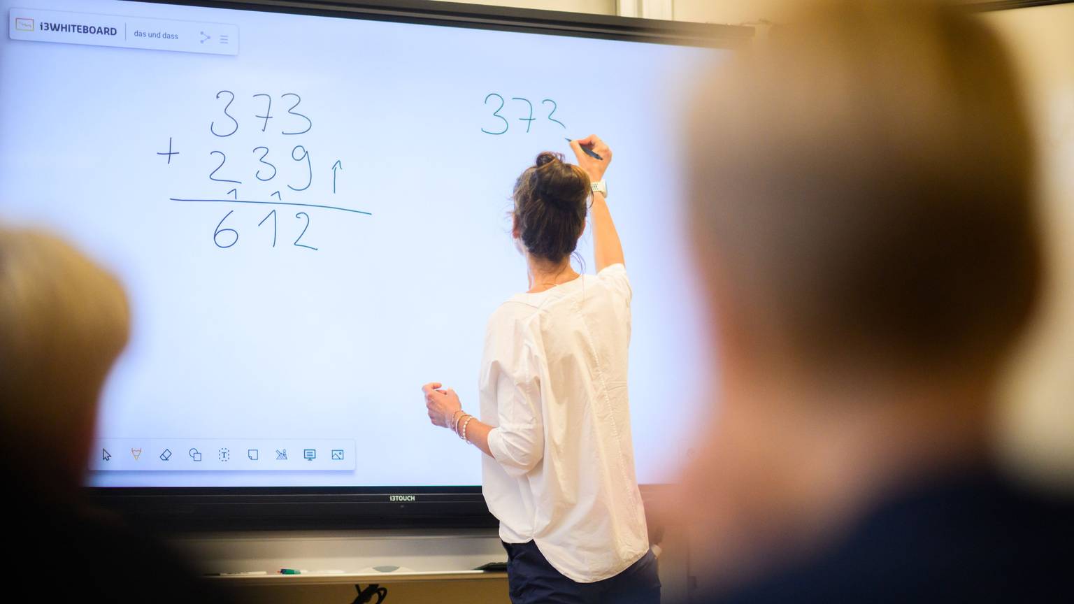 Eine Lehrerin schreibt eine Mathematikaufgabe auf eine digitale Schultafel (Symbolbild)