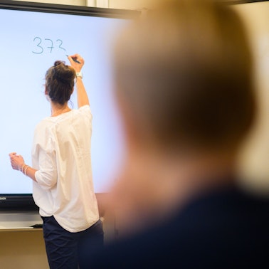 Eine Lehrerin schreibt eine Mathematikaufgabe auf eine digitale Schultafel (Symbolbild)