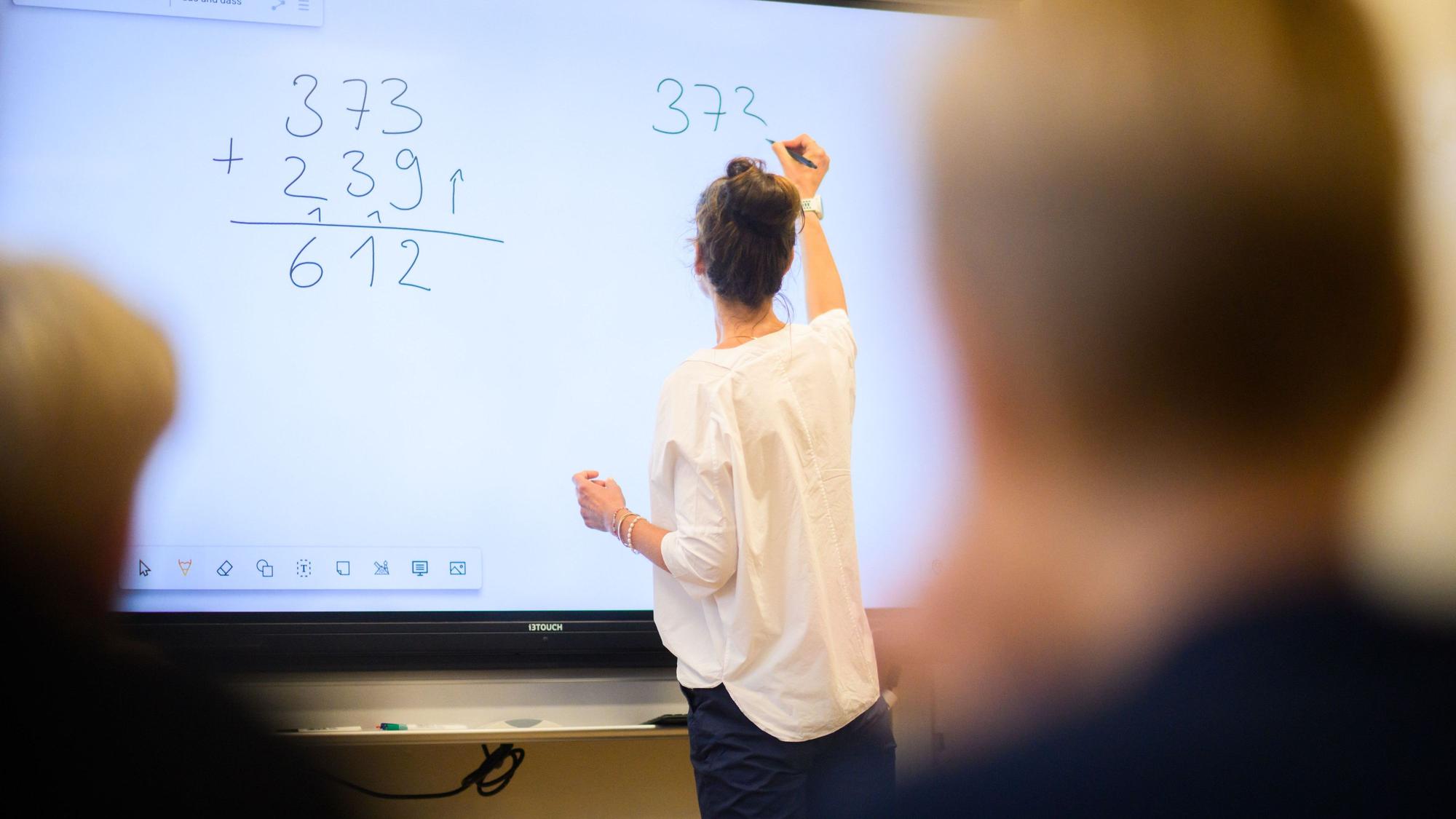 Eine Lehrerin schreibt eine Mathematikaufgabe auf eine digitale Schultafel (Symbolbild)