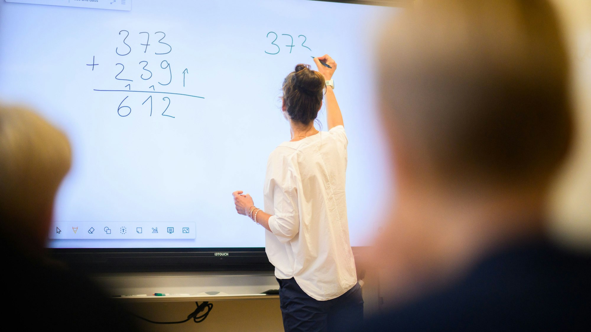 Eine Lehrerin schreibt eine Mathematikaufgabe auf eine digitale Schultafel (Symbolbild)