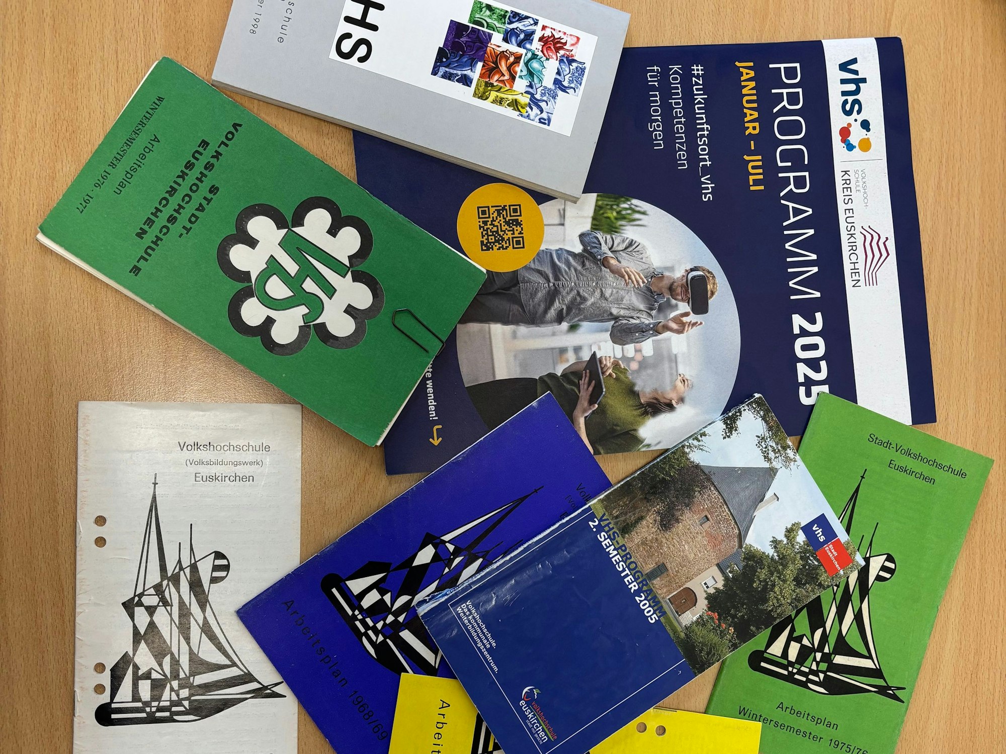 Kurshefte der VHS Kreis Euskirchen aus verschiedenen Jahrzehnten liegen auf einem Tisch. Die Hefte überlagern sich.