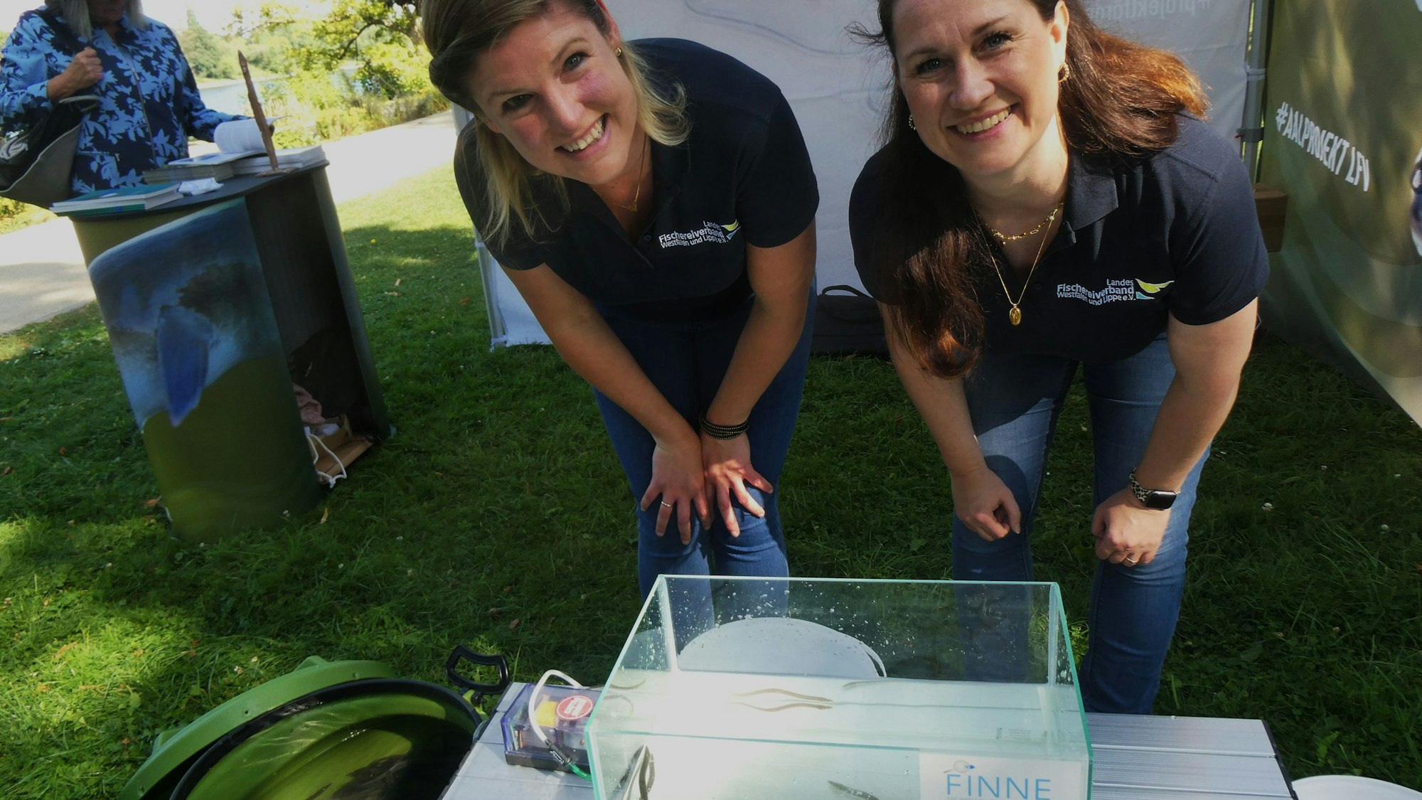 Zwei Frauen mit einem kleinen Wasserbecken, in dem junge Aale schwimmen.