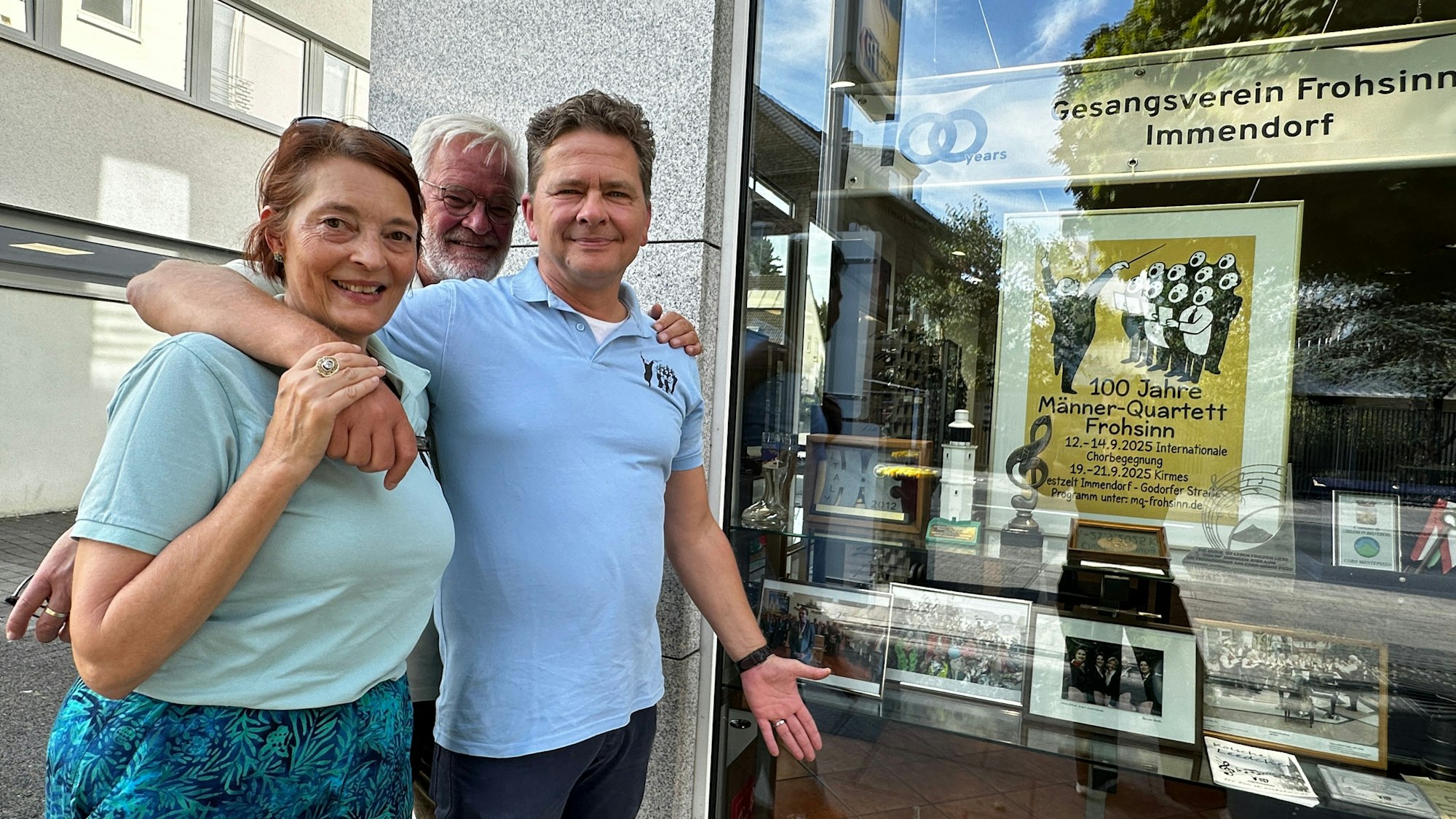 Eine Frau und zwei Männer stehen vor einem Schaufenster, das zum Thema 100 Jahre Männer-Quartett Frohsinn dekoriert ist.