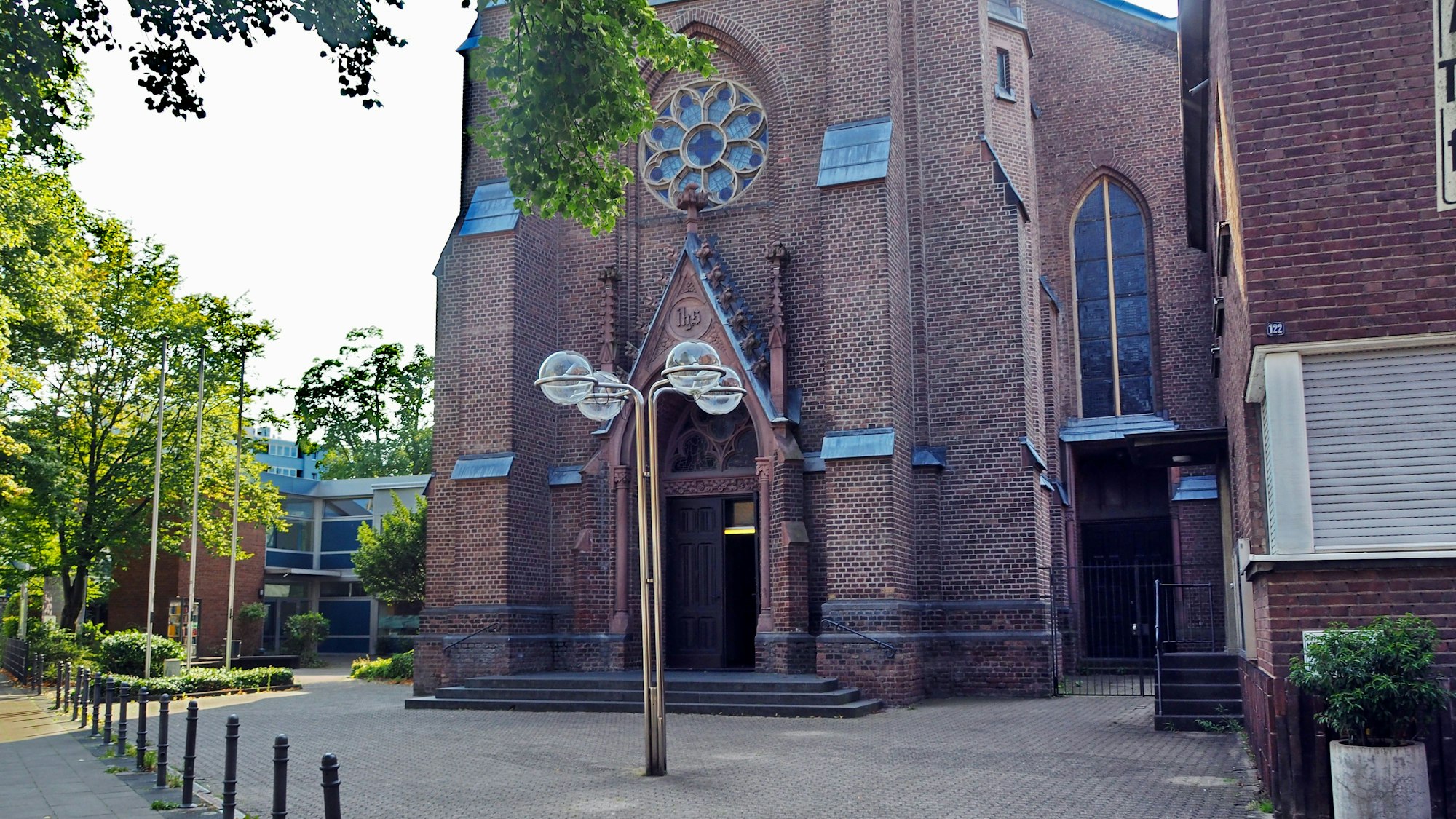 Vor einer Kirche steht eine Laterne, daneben ein Haus ebenso aus rötlichem Backstein gebaut.