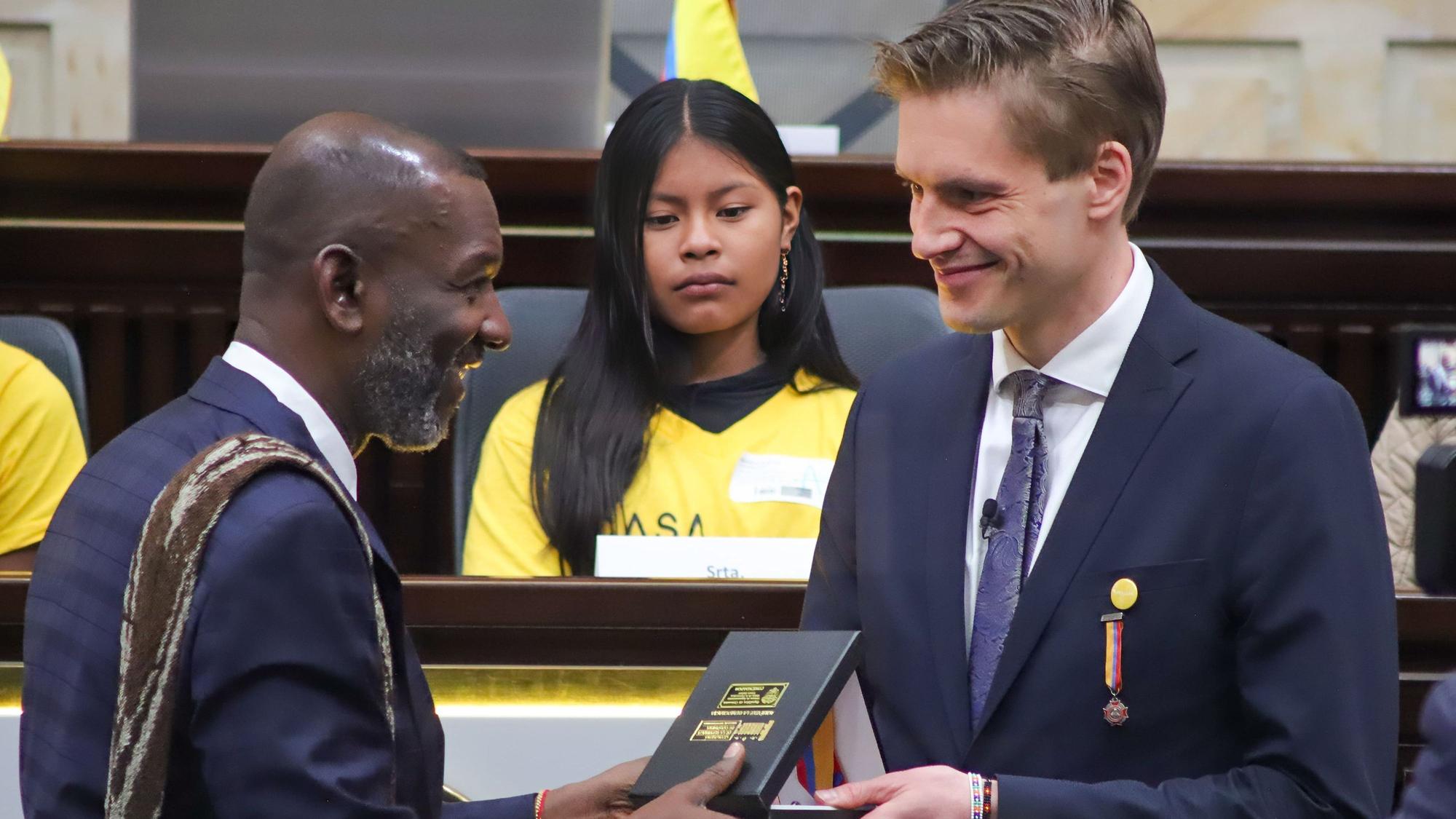 Dr. James Nosquero Torres überreicht Dr.Theo Rüber den hohen Orden im kolumbianischen Parlament in Bogota. Im Hintergrund sitzt eines der Mädchen, die in einem der Wohnheime von Casa Hogar lebt.