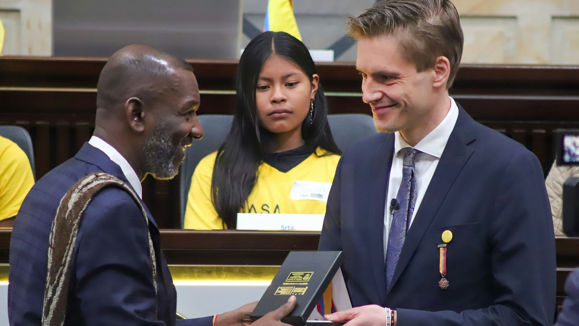 Dr. James Nosquero Torres überreicht Dr.Theo Rüber den hohen Orden im kolumbianischen Parlament in Bogota. Im Hintergrund sitzt eines der Mädchen, die in einem der Wohnheime von Casa Hogar lebt.