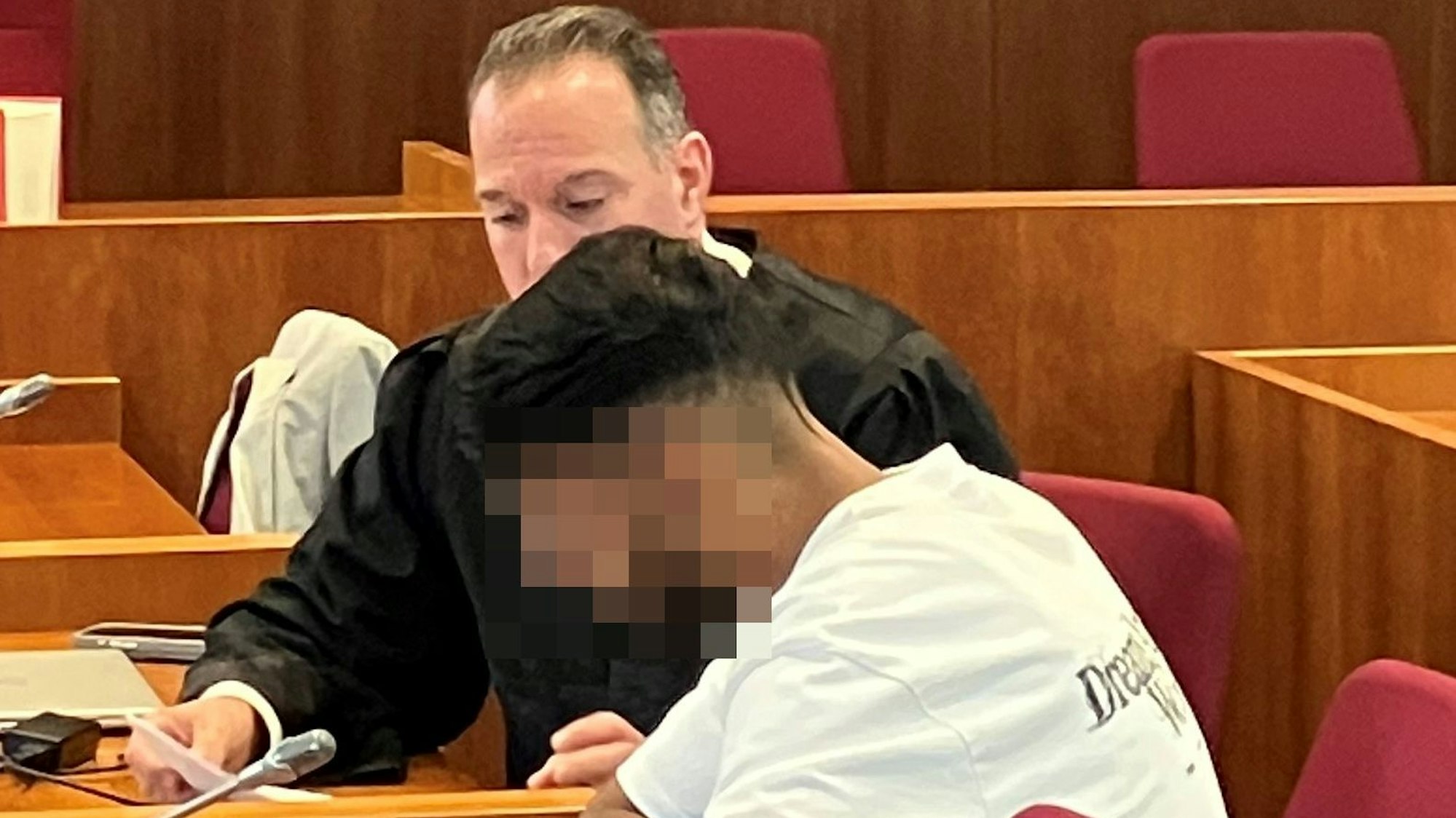 Das Bild zeigt den Angeklagten, dessen Gesicht unkenntlich gemacht wurde, und im Hintergrund einen Anwalt.