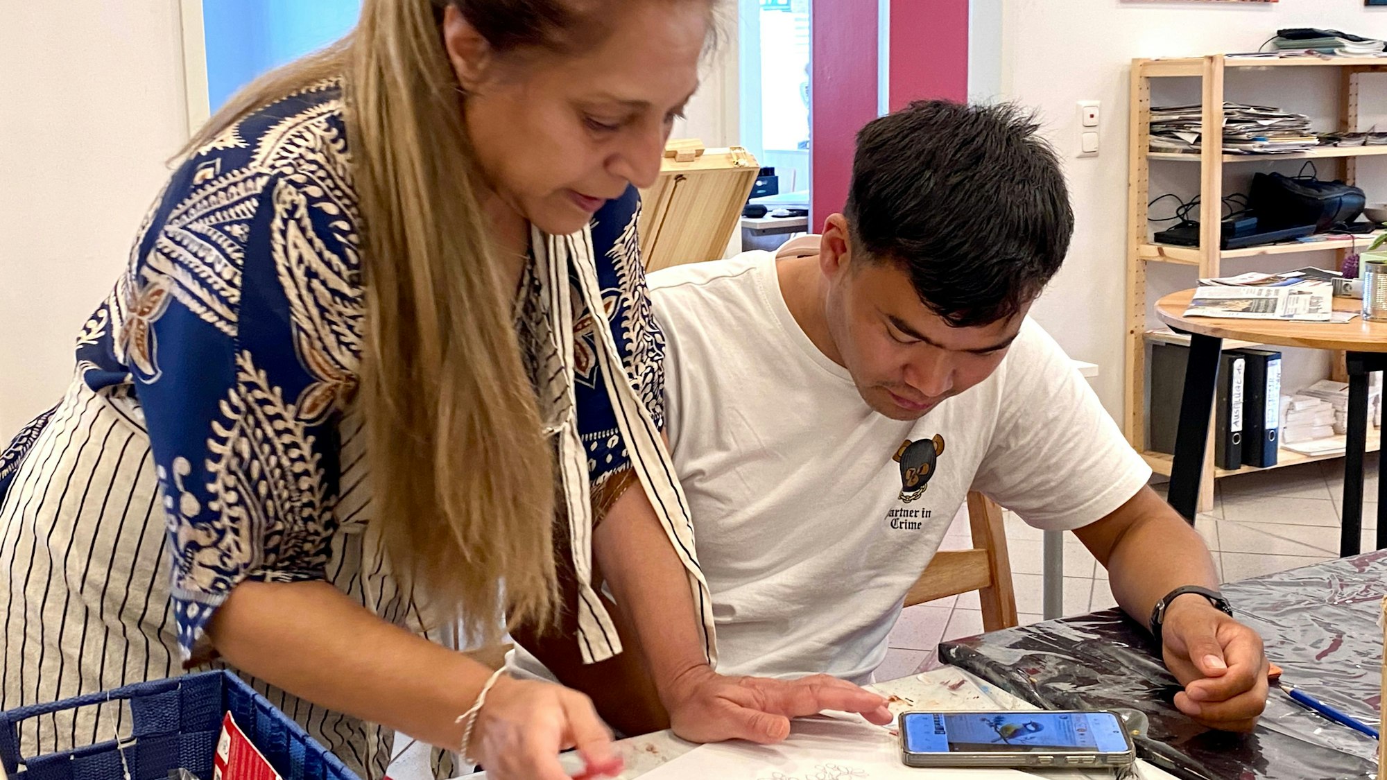 Eine Frau steht neben einem jungen Mann , der auf seinem Handy nach einem Zeichenmotiv sucht.