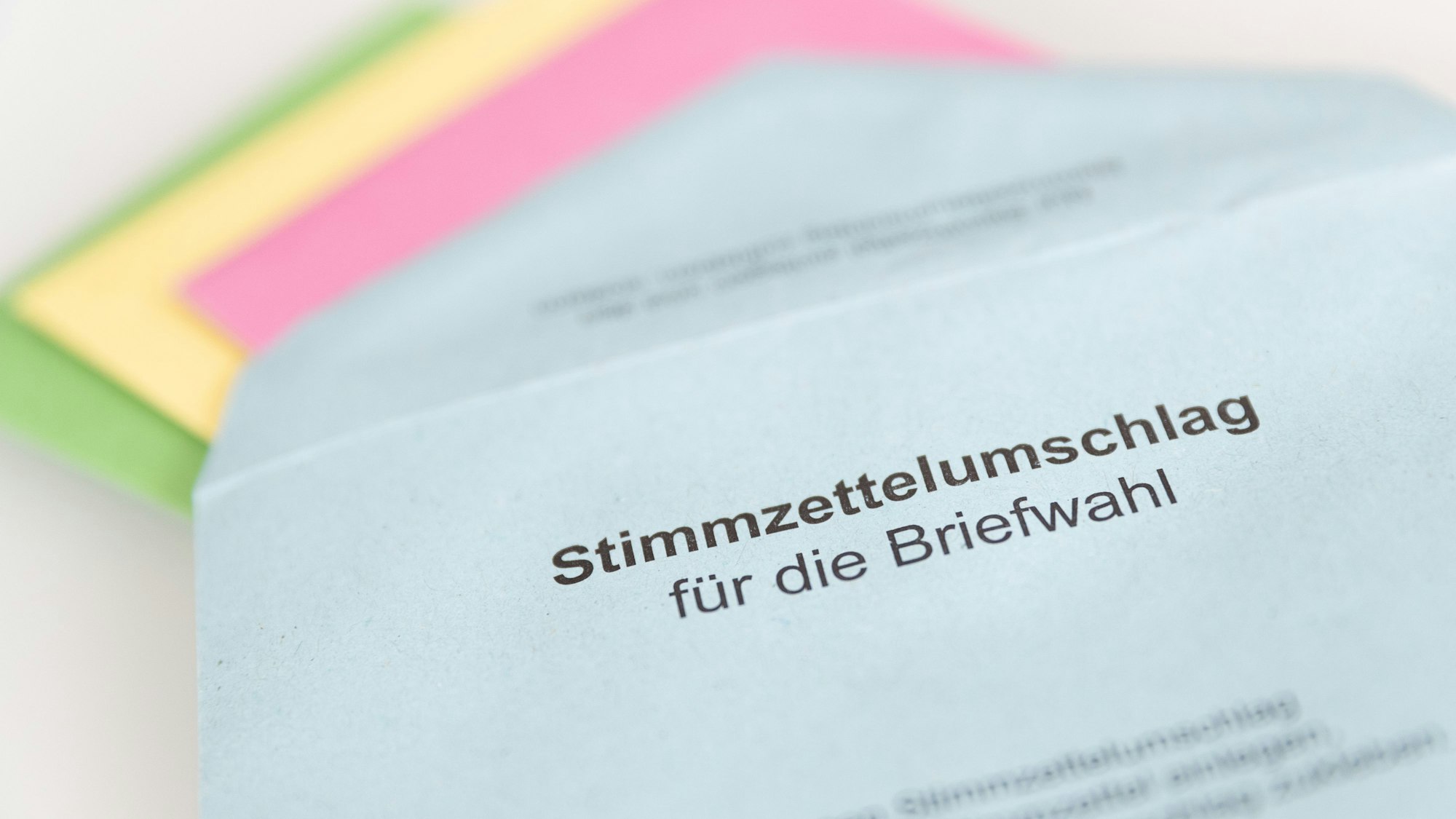 Ein Stimmzettelumschlag für die Briefwahl, aus dem verschiedenfarbige Stimmzettel rausgezogen wurden.
