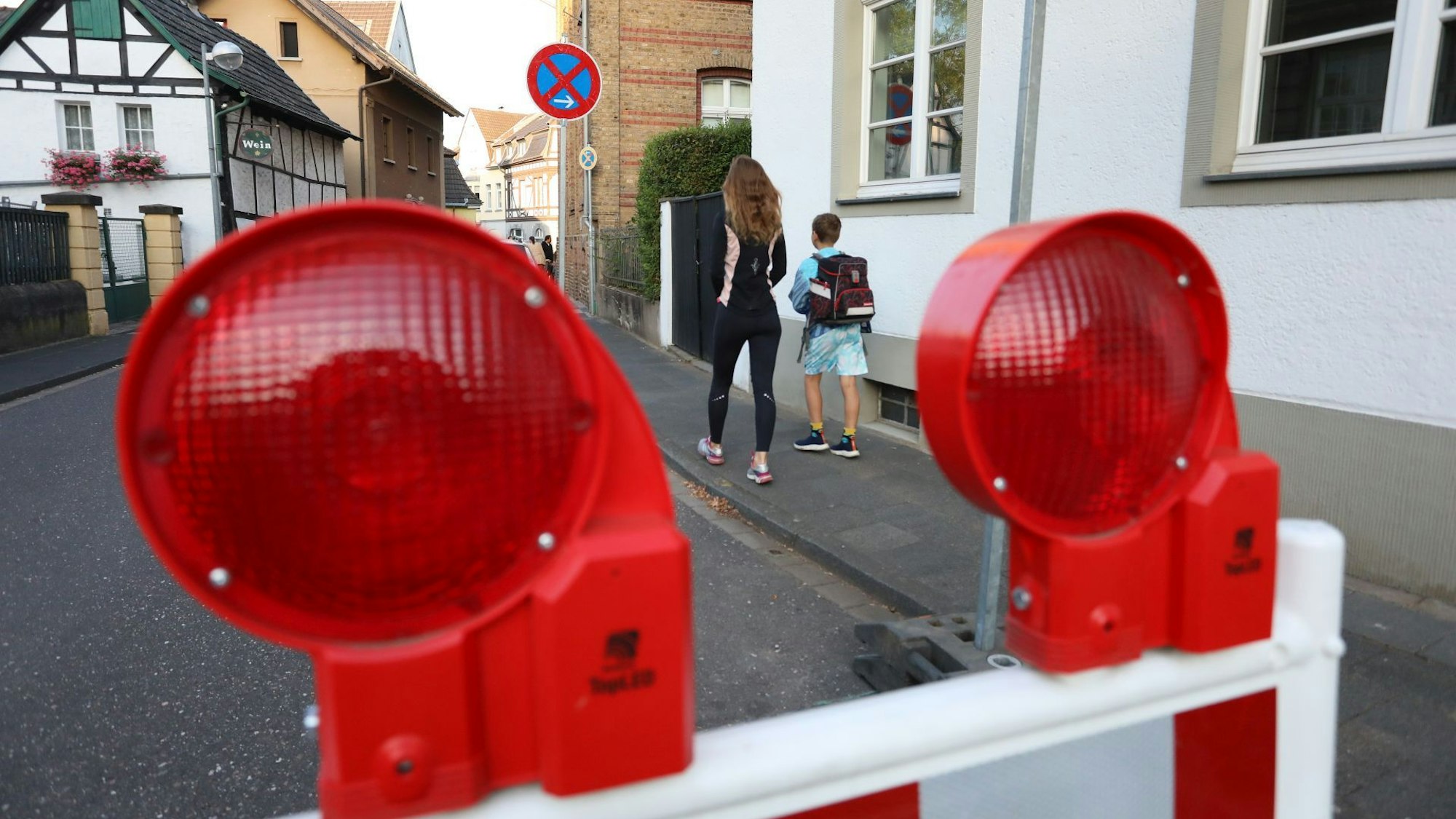 Eine Sperrbake mit roten Lampen auf einer Straße, im Hintergrund eine Mutter mit ihrem Kind