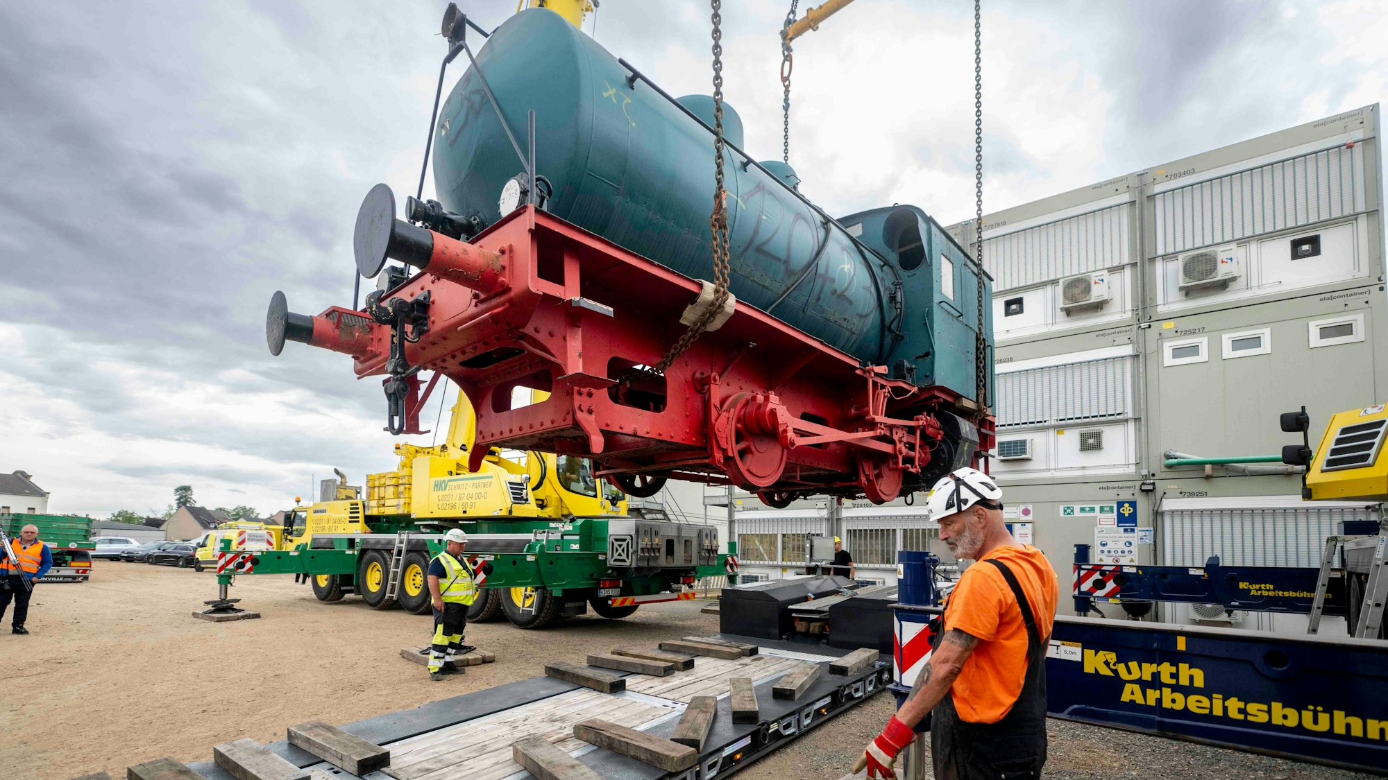 Das Bild zeigt die grün-rote Lok am Haken. Mitarbeiter des Spezialunternehmens kontrollieren die Verhebe-Akion.