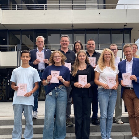 Eine Gruppe Erwachsener und Jugendlicher steht vor dem Euskirchener Kreishaus und hält Broschüren vor sich.