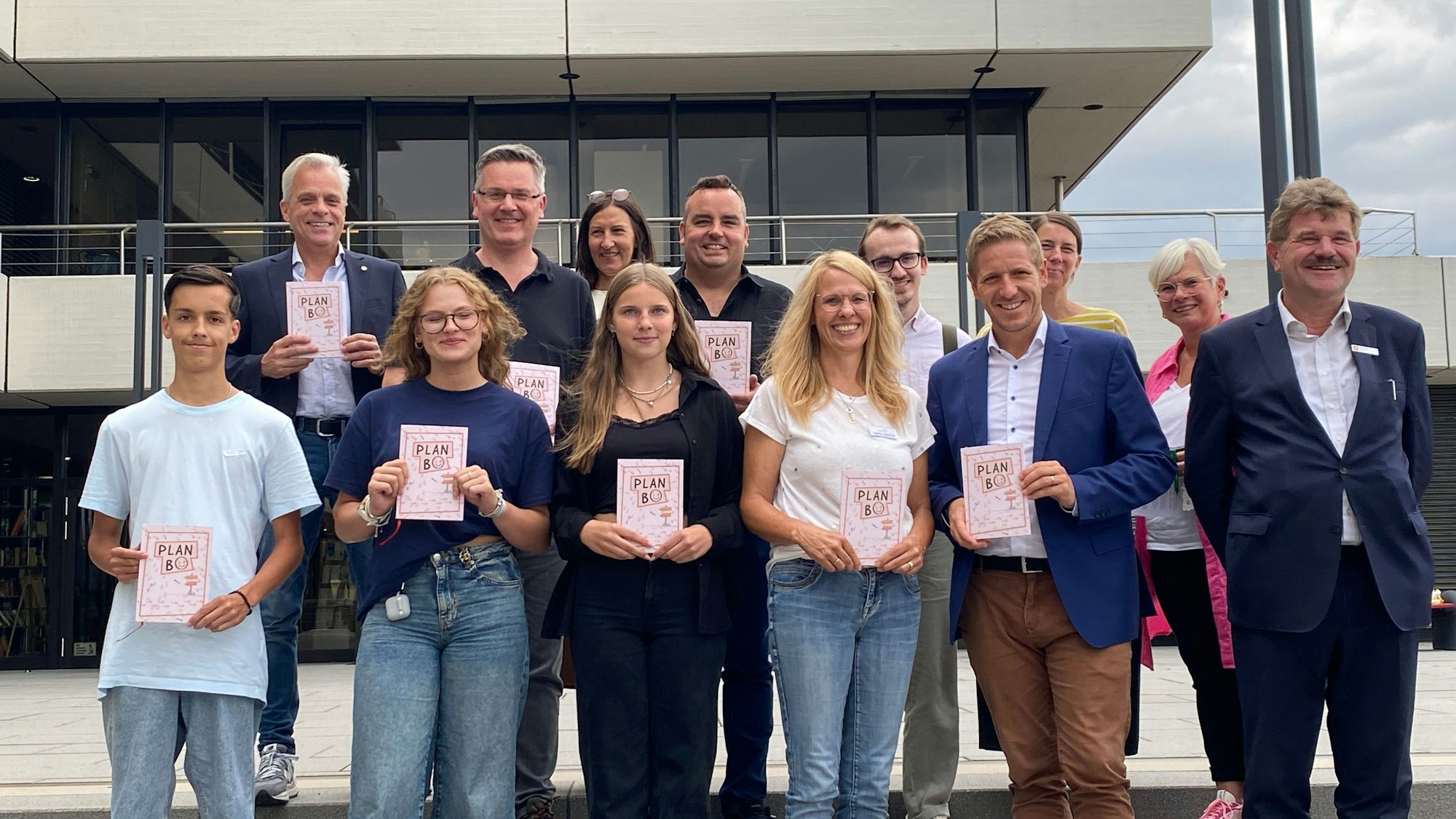 Eine Gruppe Erwachsener und Jugendlicher steht vor dem Euskirchener Kreishaus und hält Broschüren vor sich.