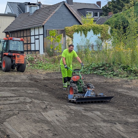 Das Foto zeigt einen Mitarbeiter der Stadtwerke beim Bearbeiten des Bodens, im Hintergrund ein Bagger.