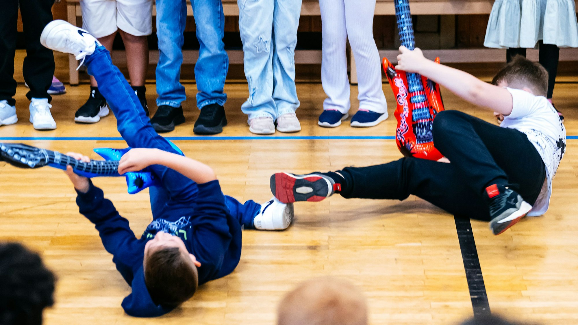 Zwei Jungen mit Plastikgitarren auf dem Turnhallenboden.