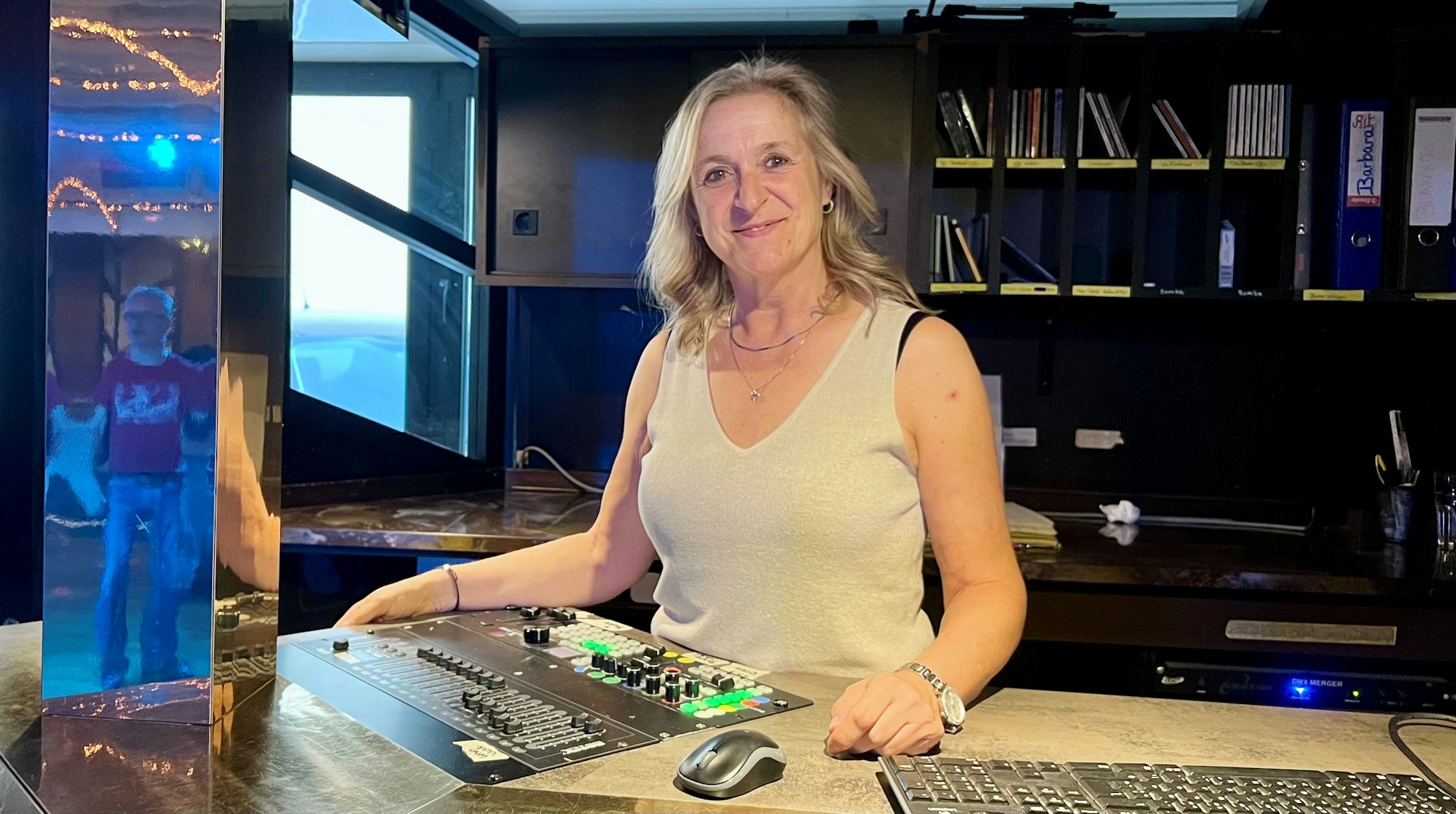 Eine Frau steht hinter einer Art Theke, auf der ein Musik-Mischpult zu sehen ist.