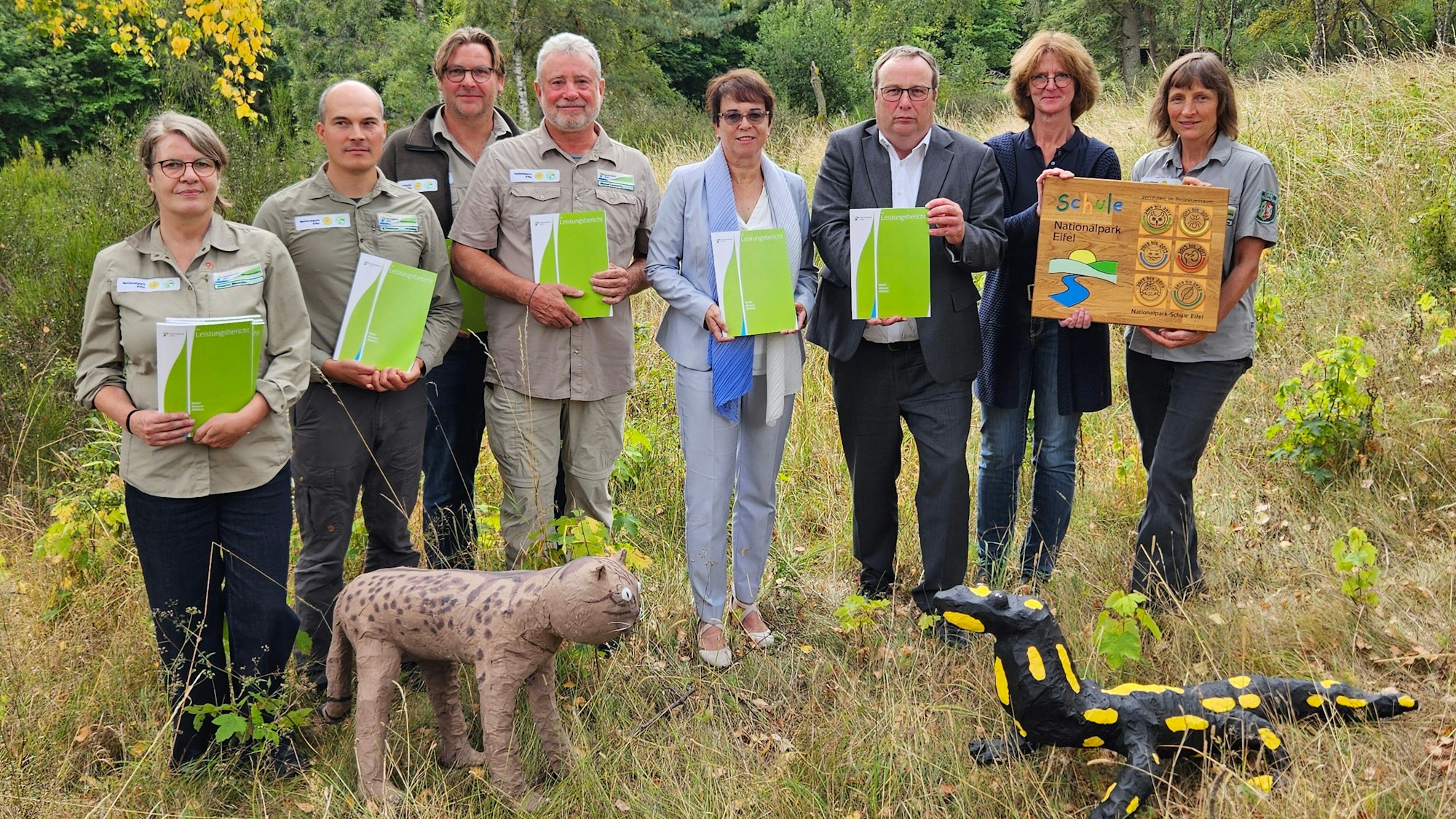 Michael Lammertz und Minister Oliver Krischer stehen mit Mitarbeitern des Parks, der Präsidentin und Lehrerin Anja Henseler nebeneinander und präsentieren den Bericht.