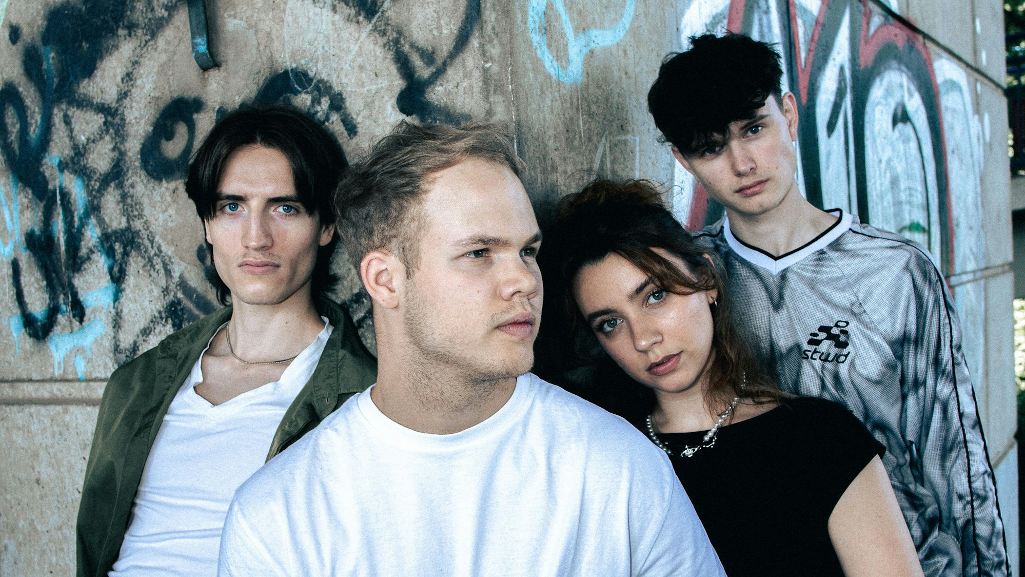 Vier junge Leute vor einer Graffiti-Wand.